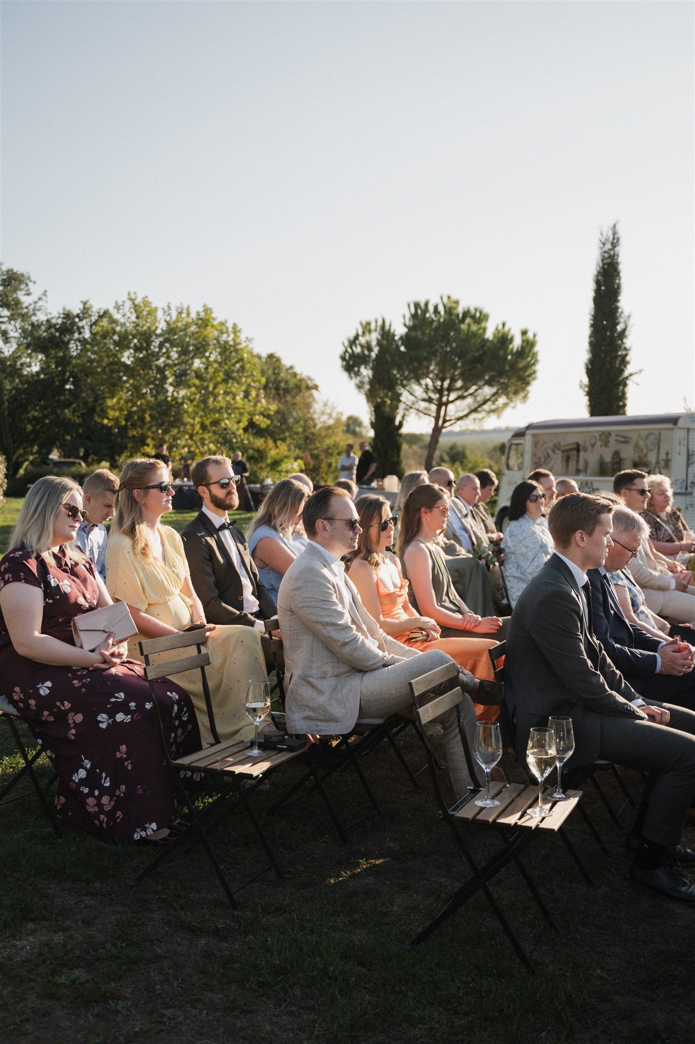 Wedding guests seated in rows of chairs during an outdoor ceremony at sunset.
