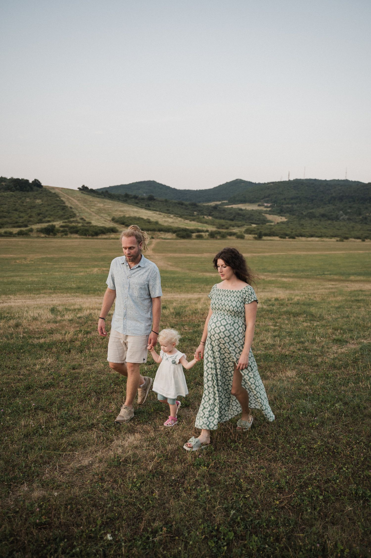 A family walks together through a grassy meadow with rolling hills in the background.