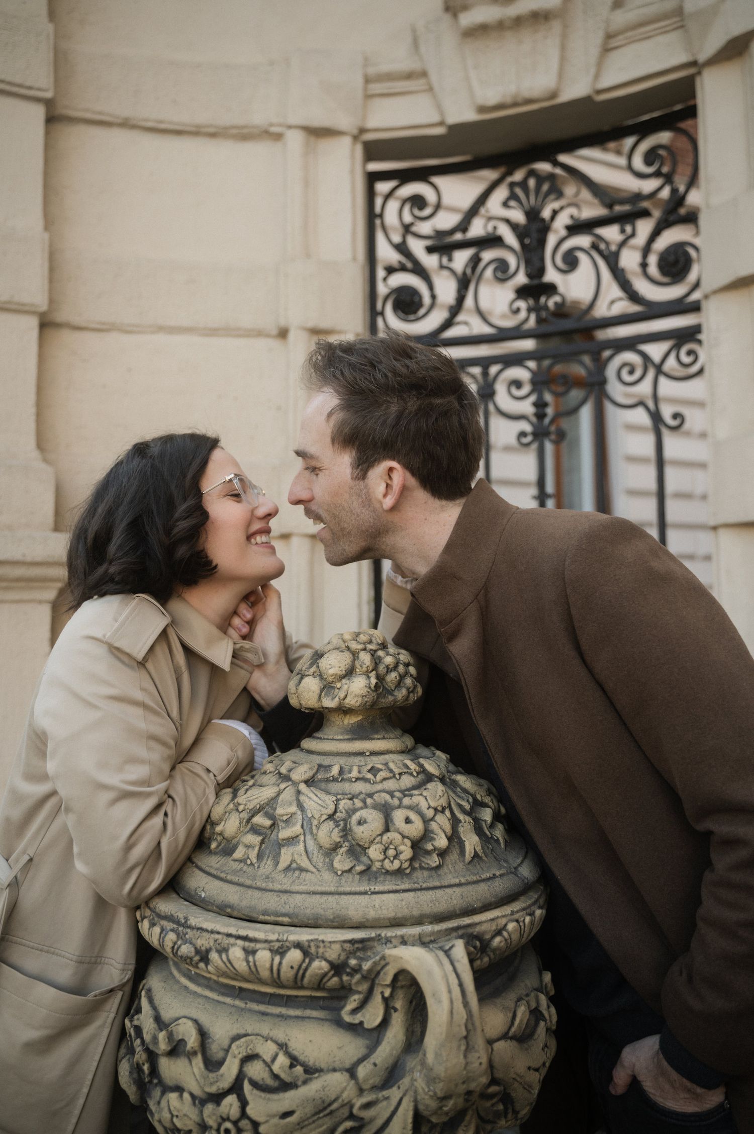 A couple shares intimate moments in a romantic photoshoot by ornate stone pillars and decorative urns.