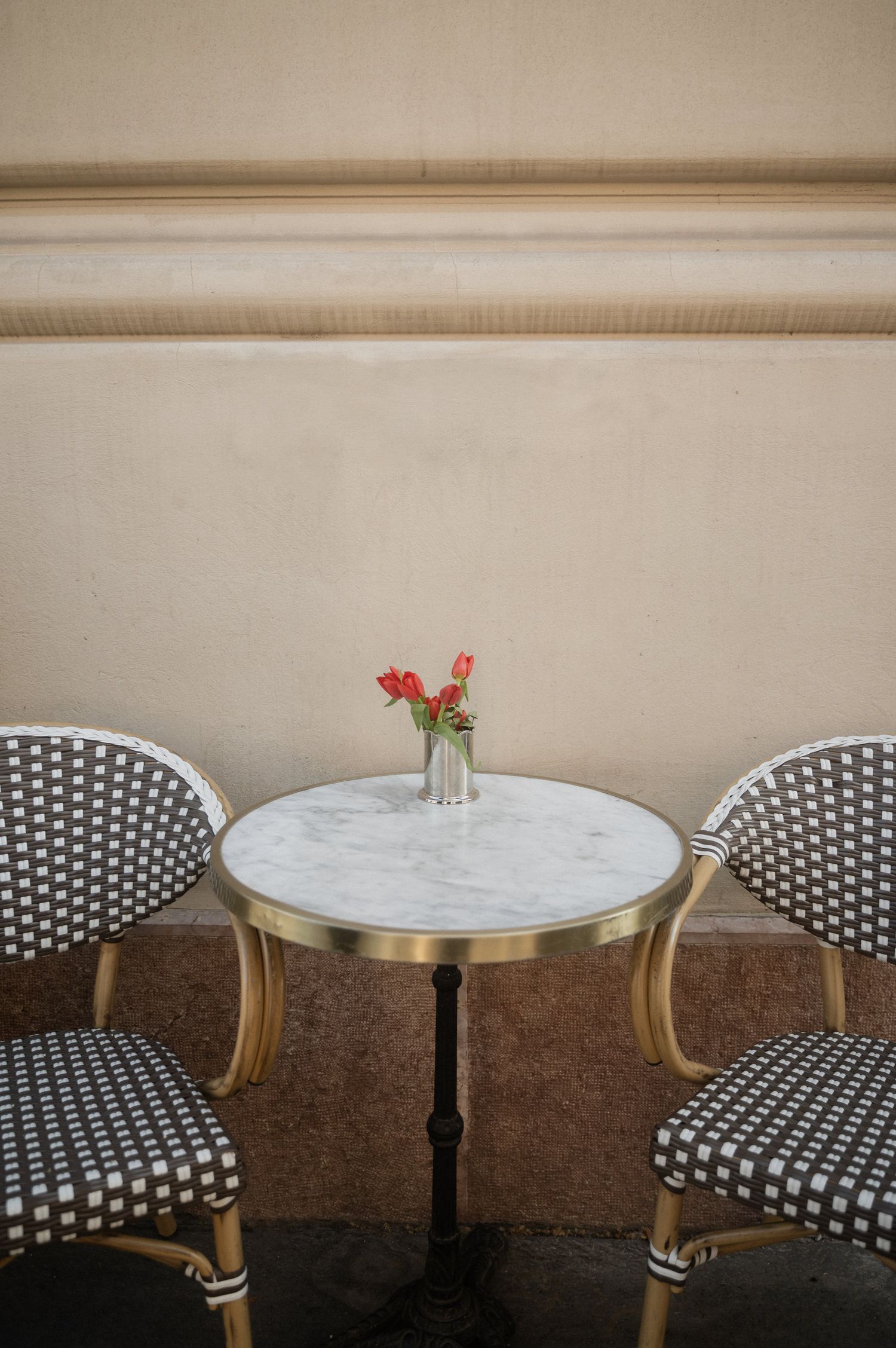Modern cafe interior with black and white checkered chairs and round marble tables against a beige wall.