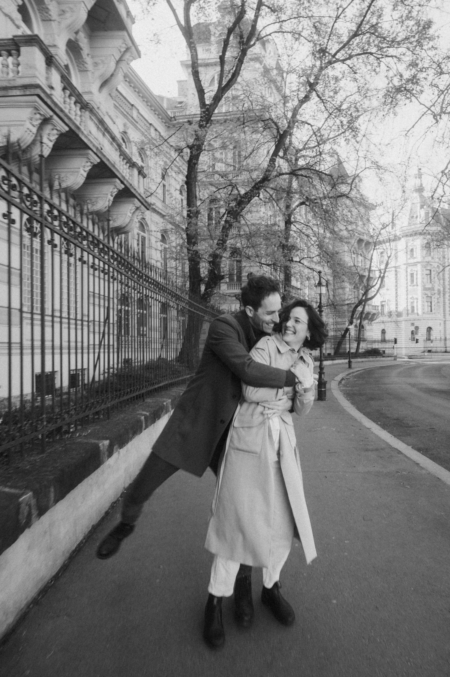 Black and white photo sequence showing playful movement and interaction along a tree-lined street with iron railings.