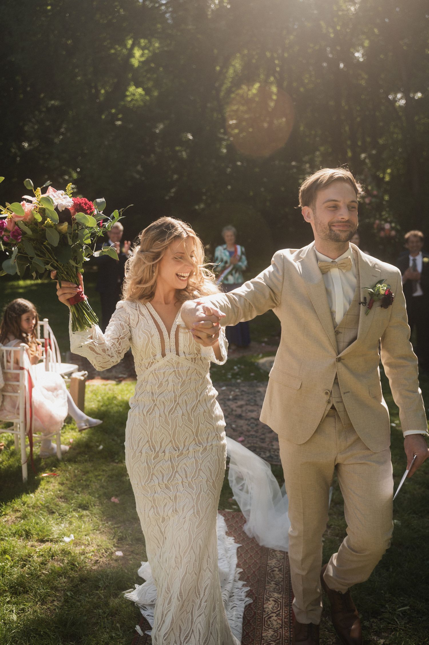 A couple in wedding attire dances joyfully together in a sunlit garden setting during their celebration.