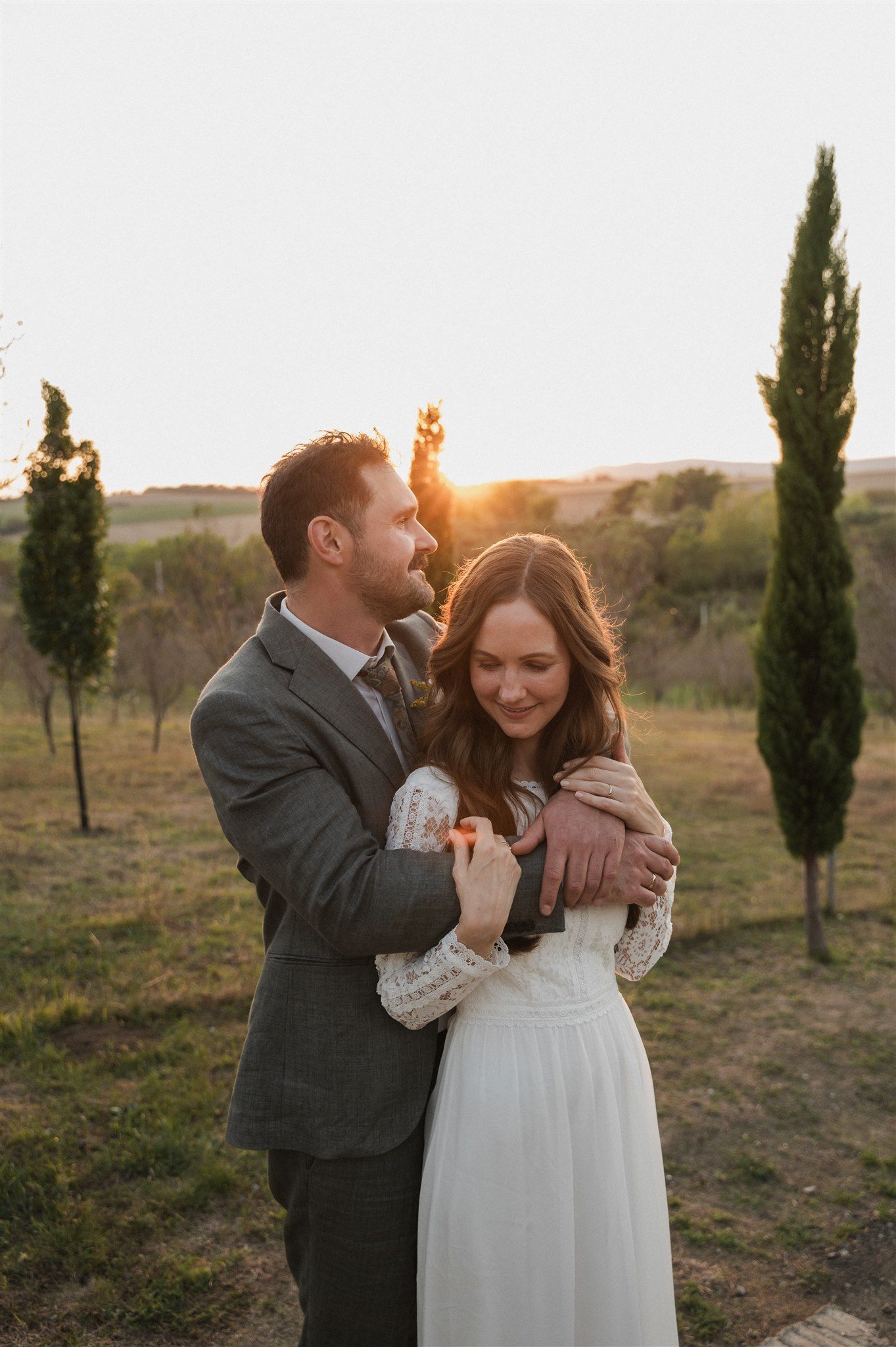 Couple shares intimate moments during sunset golden hour portraits among cypress trees.