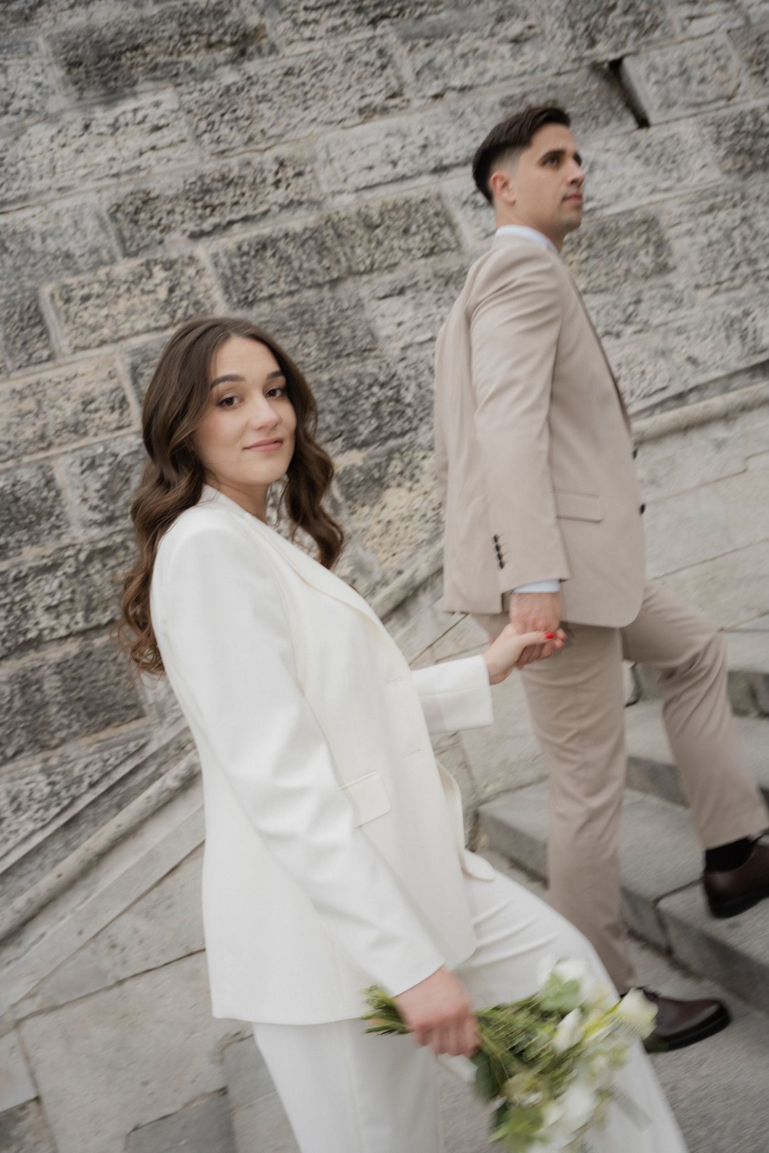 A man and a woman in formal attire stand together against a brick wall.