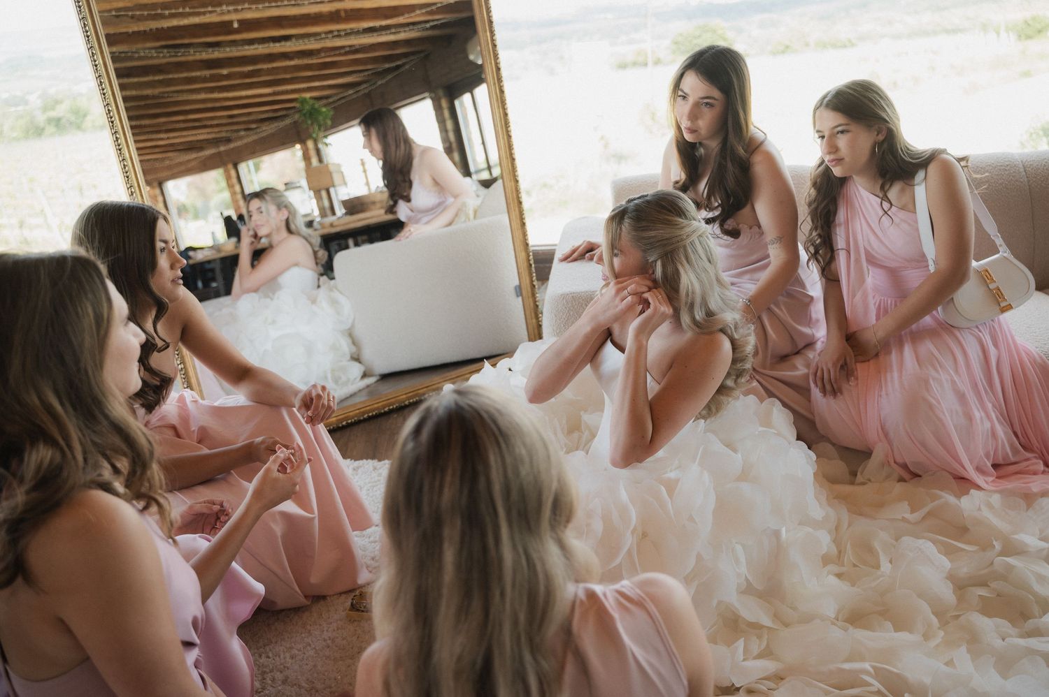 Bride in white gown surrounded by bridesmaids in pink dresses sharing an emotional moment before the wedding ceremony.