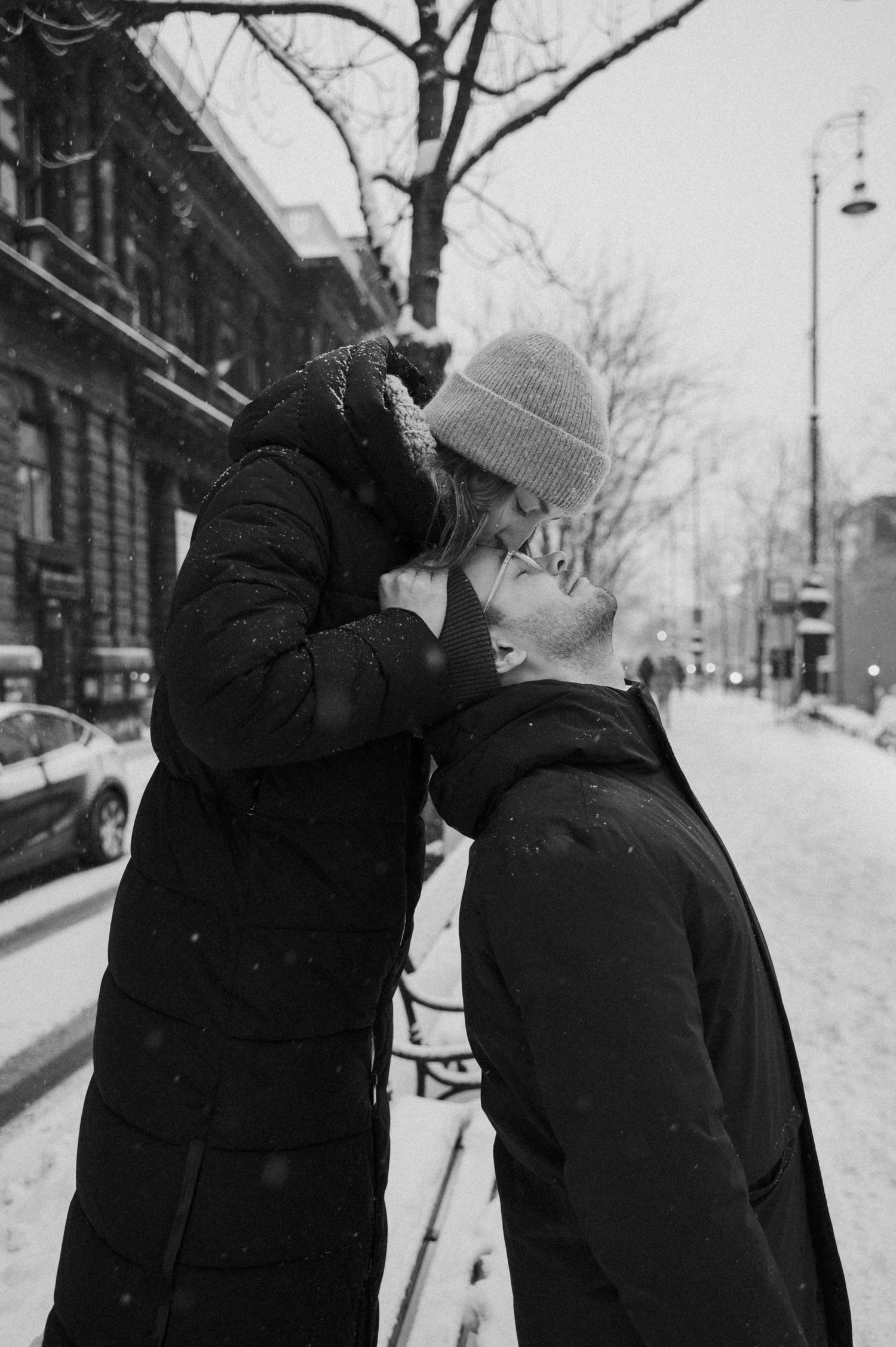 A romantic winter moment between two people sharing a kiss on a snowy city street.
