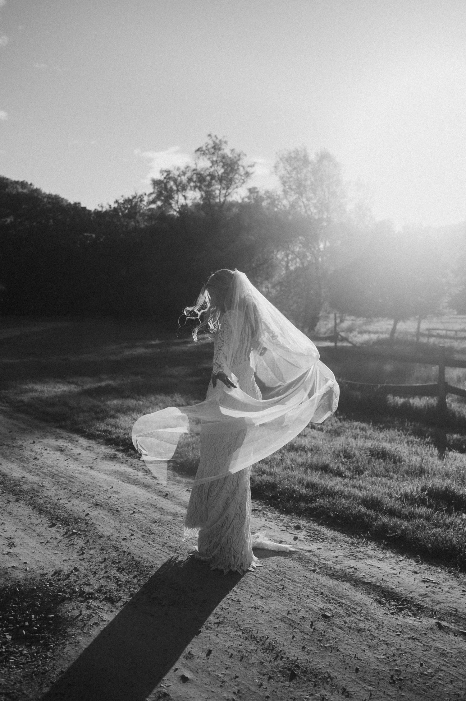 A flowing white veil catches sunlight as it billows in the wind against a pastoral hillside landscape.