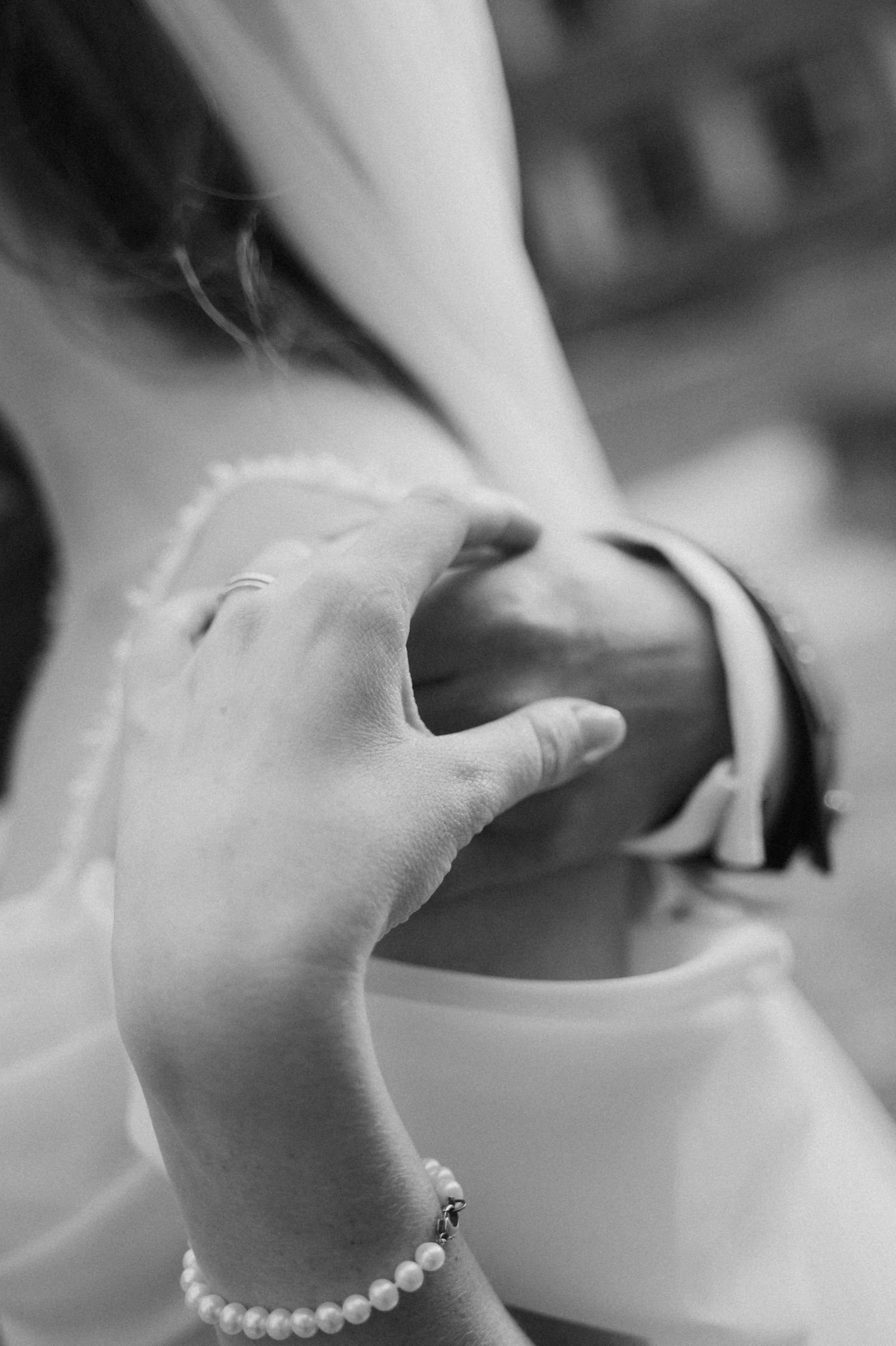 Close-up black and white photo of a bride wearing a pearl bracelet holding her grooms arm.