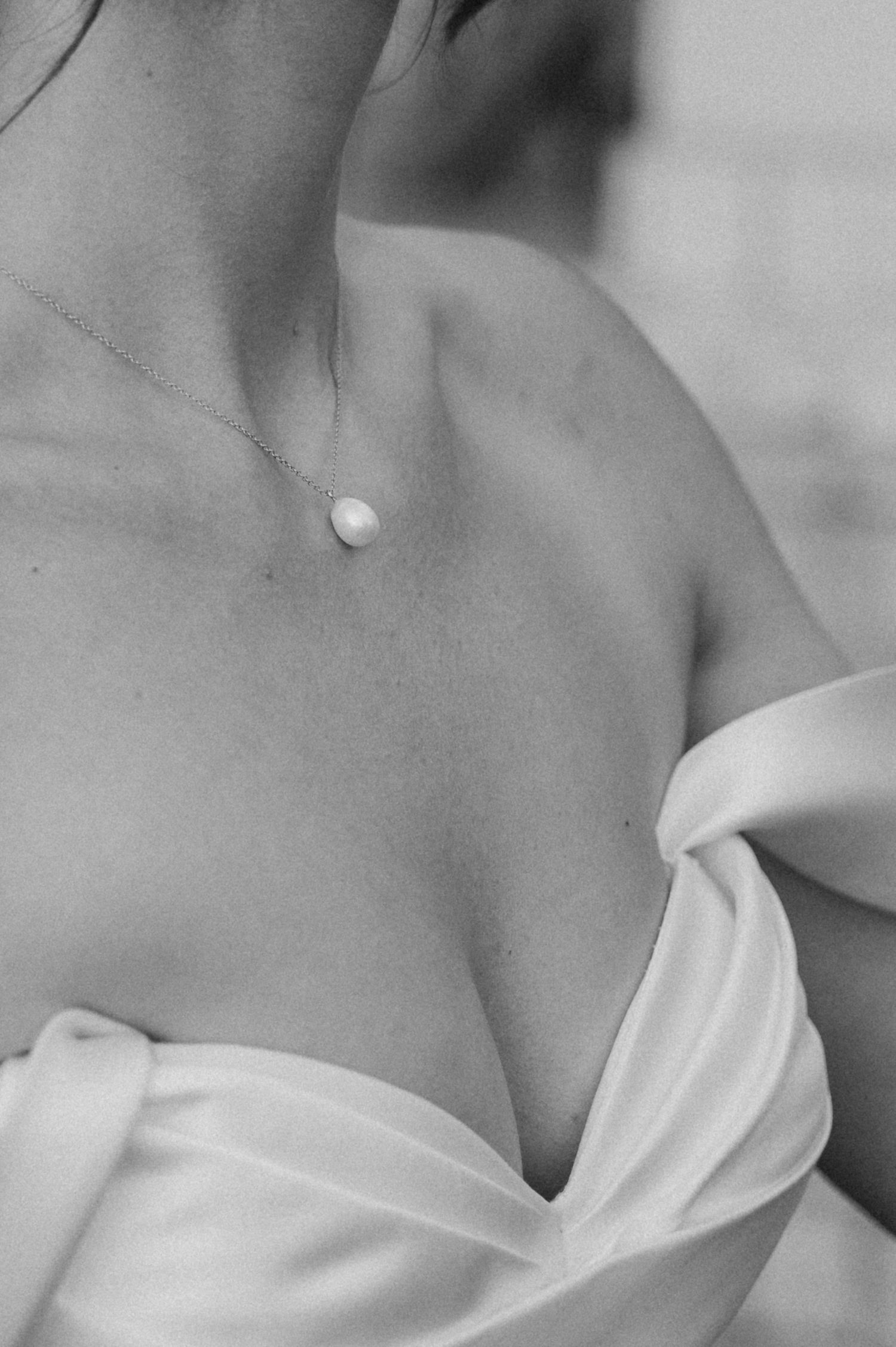 Close-up detail of a delicate pearl necklace against a wedding dress neckline in black and white.
