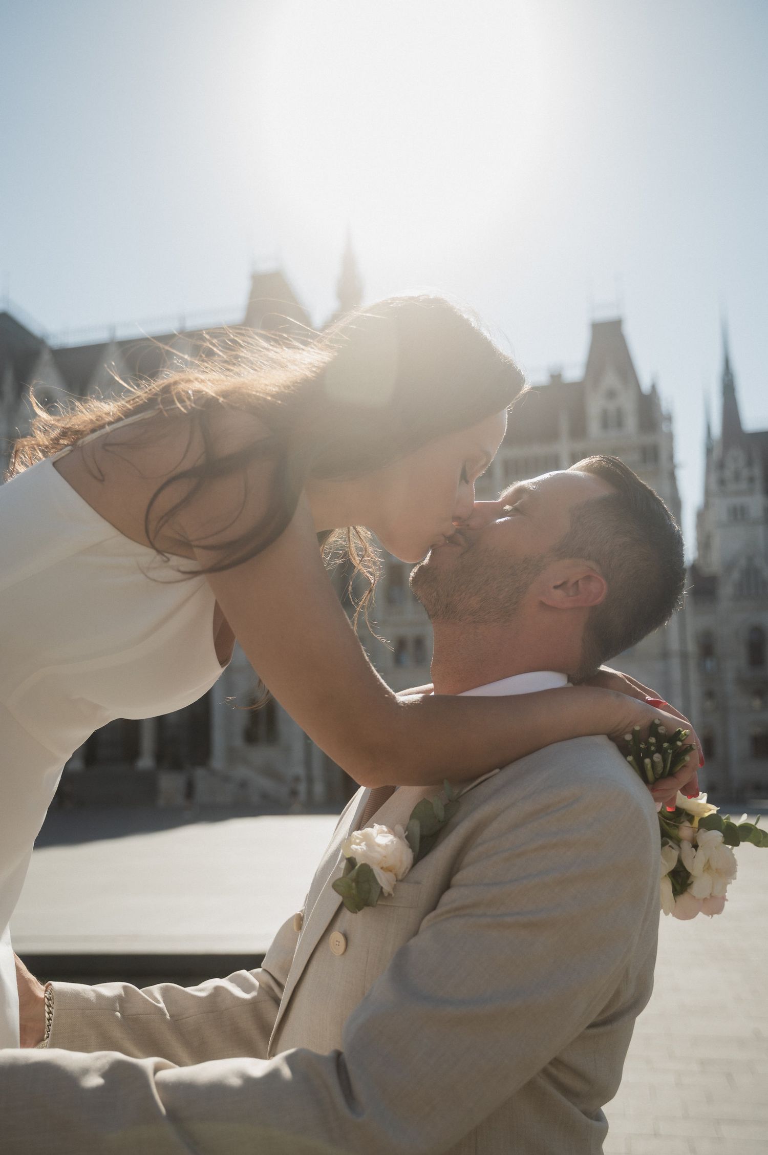 A romantic sunlit moment between newlyweds with gothic architecture in the background.