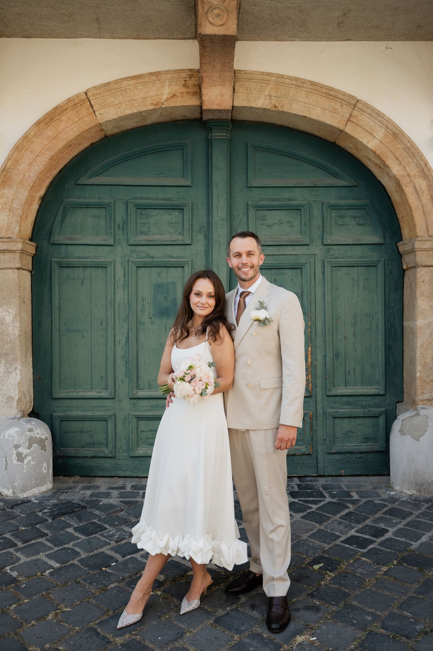 Wedding couple poses in front of an ornate green door and stone archway.