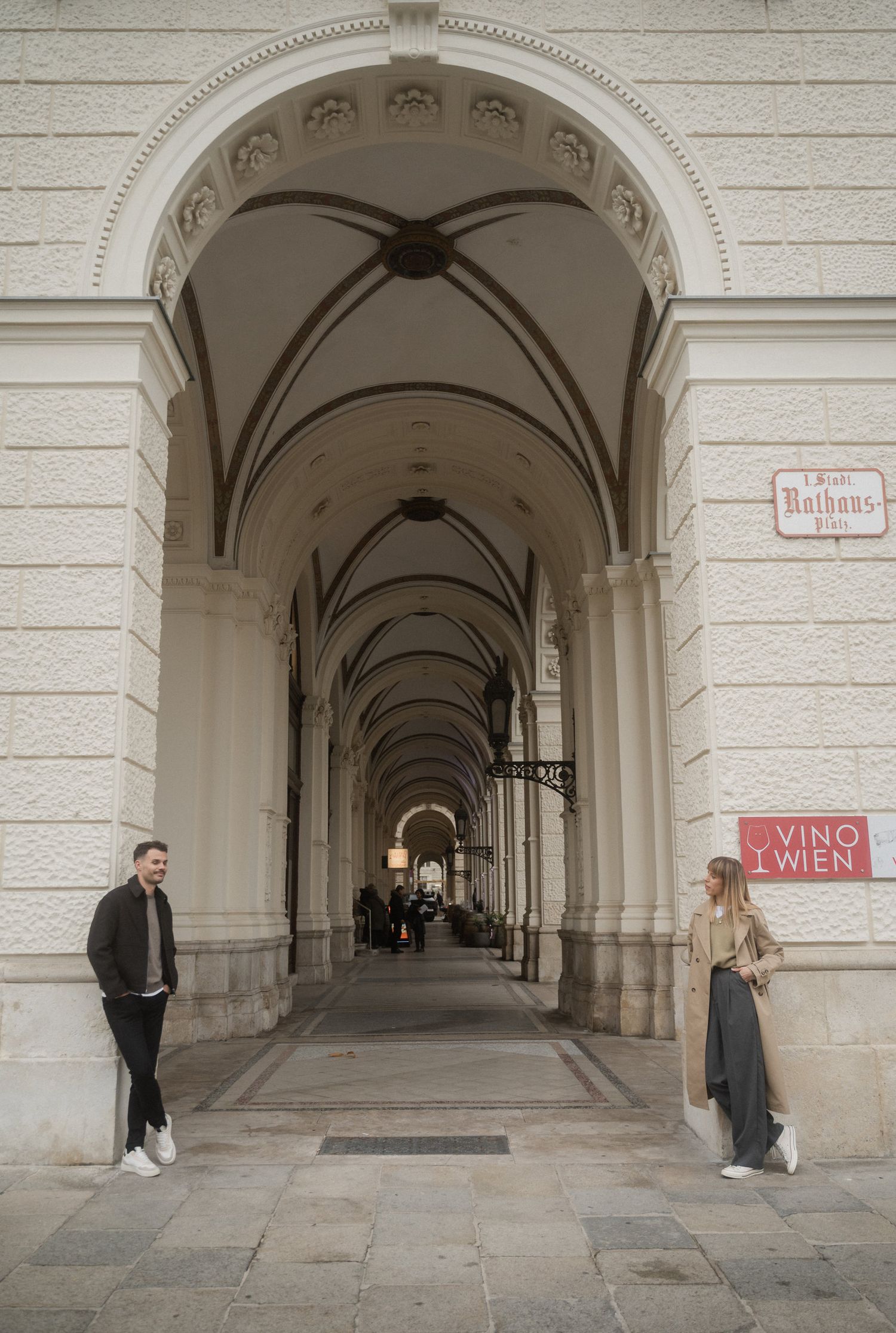 Elegant arched colonnade walkway in Vienna with classical architecture and red signage on white stone walls.