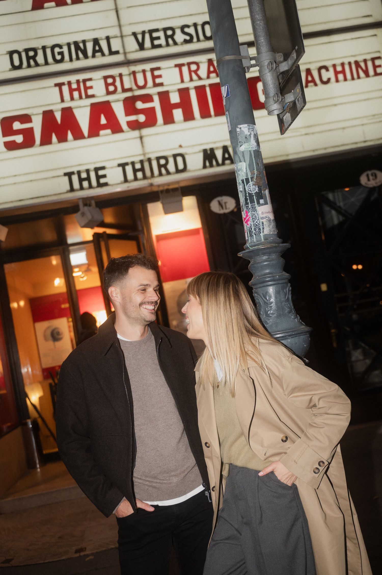 A couple shares a laugh while standing outside a theater with 