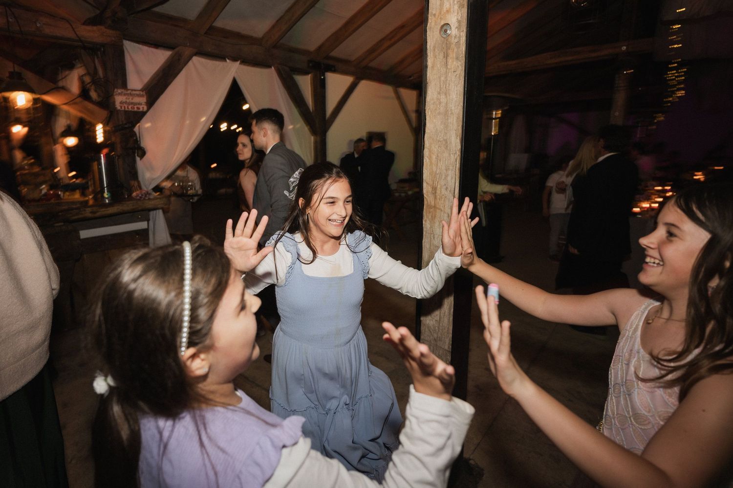 Party guests dancing and having fun at a rustic barn reception with wooden beams and dim lighting.