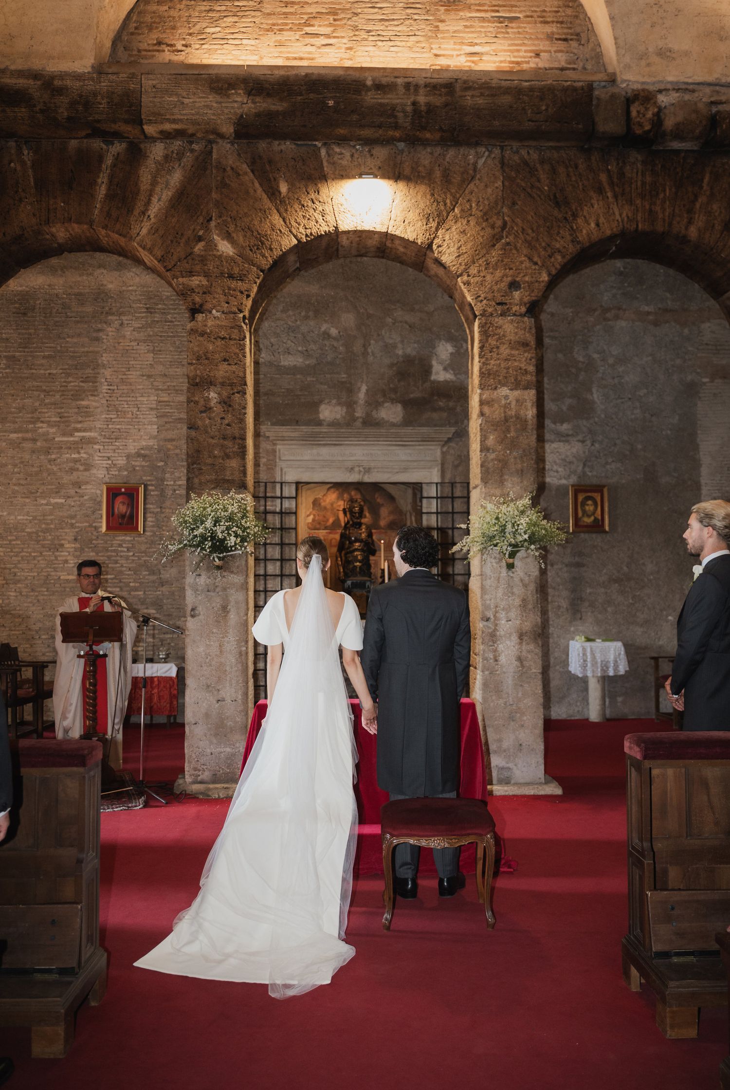 Wedding ceremony in ancient stone chapel with arched columns and red carpet.