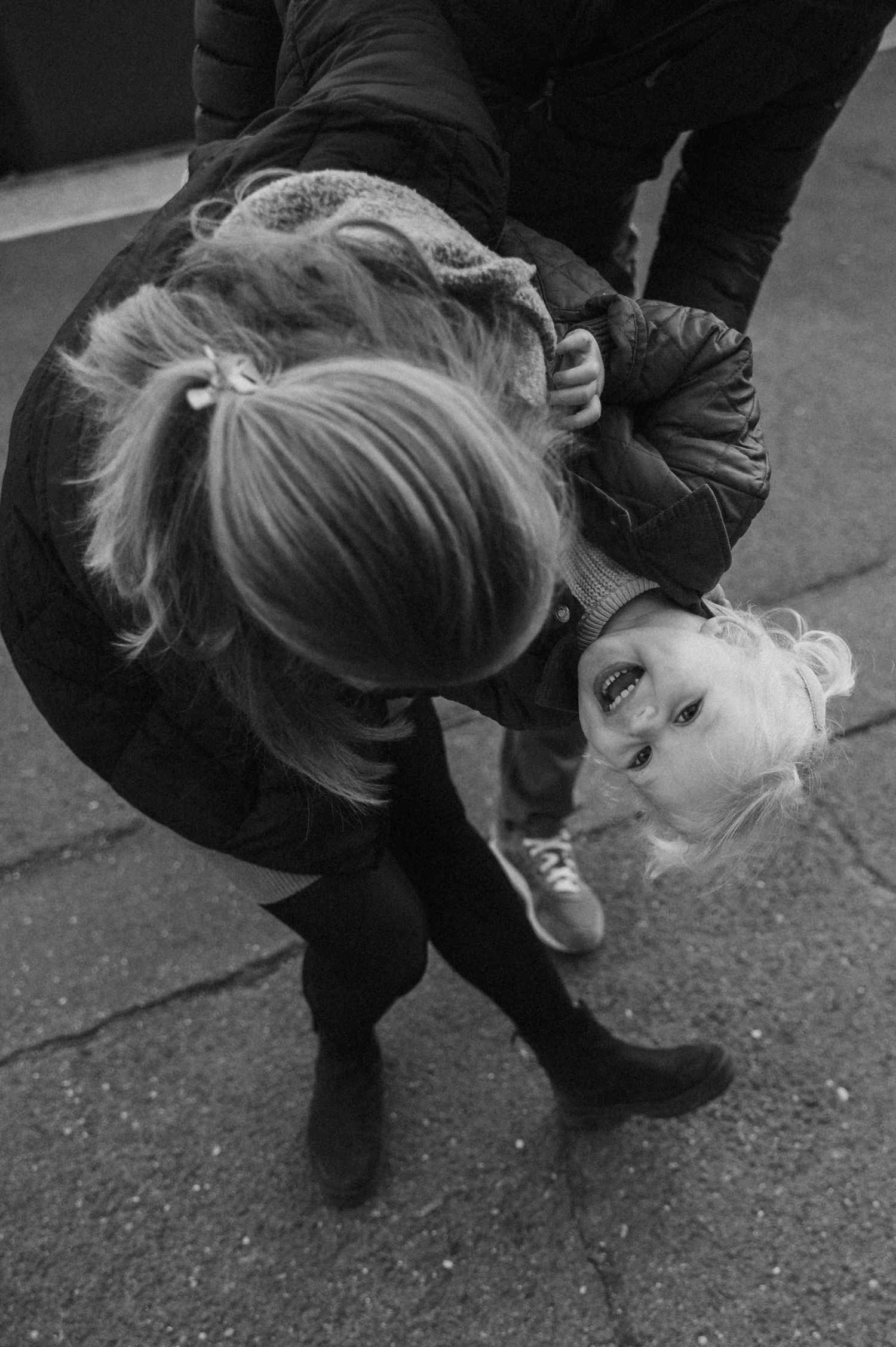 A black and white artistic photograph of a person bending backwards in a playful pose on pavement.