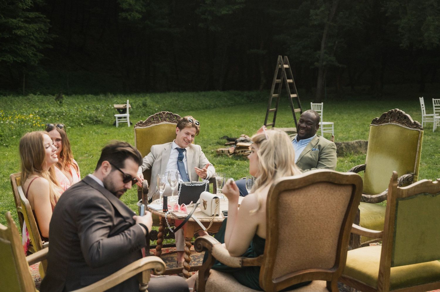 A group enjoys outdoor dining at a long table set up on a grassy lawn during a sunny afternoon gathering.
