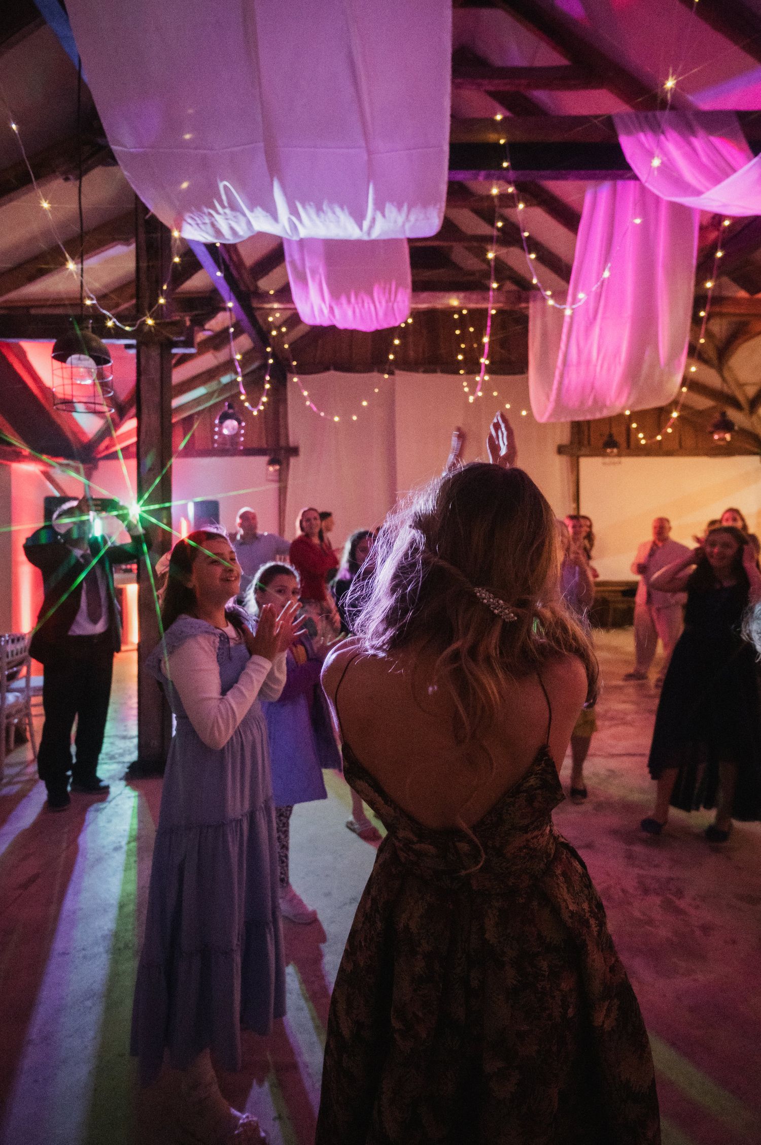 People dancing at a party venue decorated with pink uplighting and fairy lights creating a festive atmosphere.