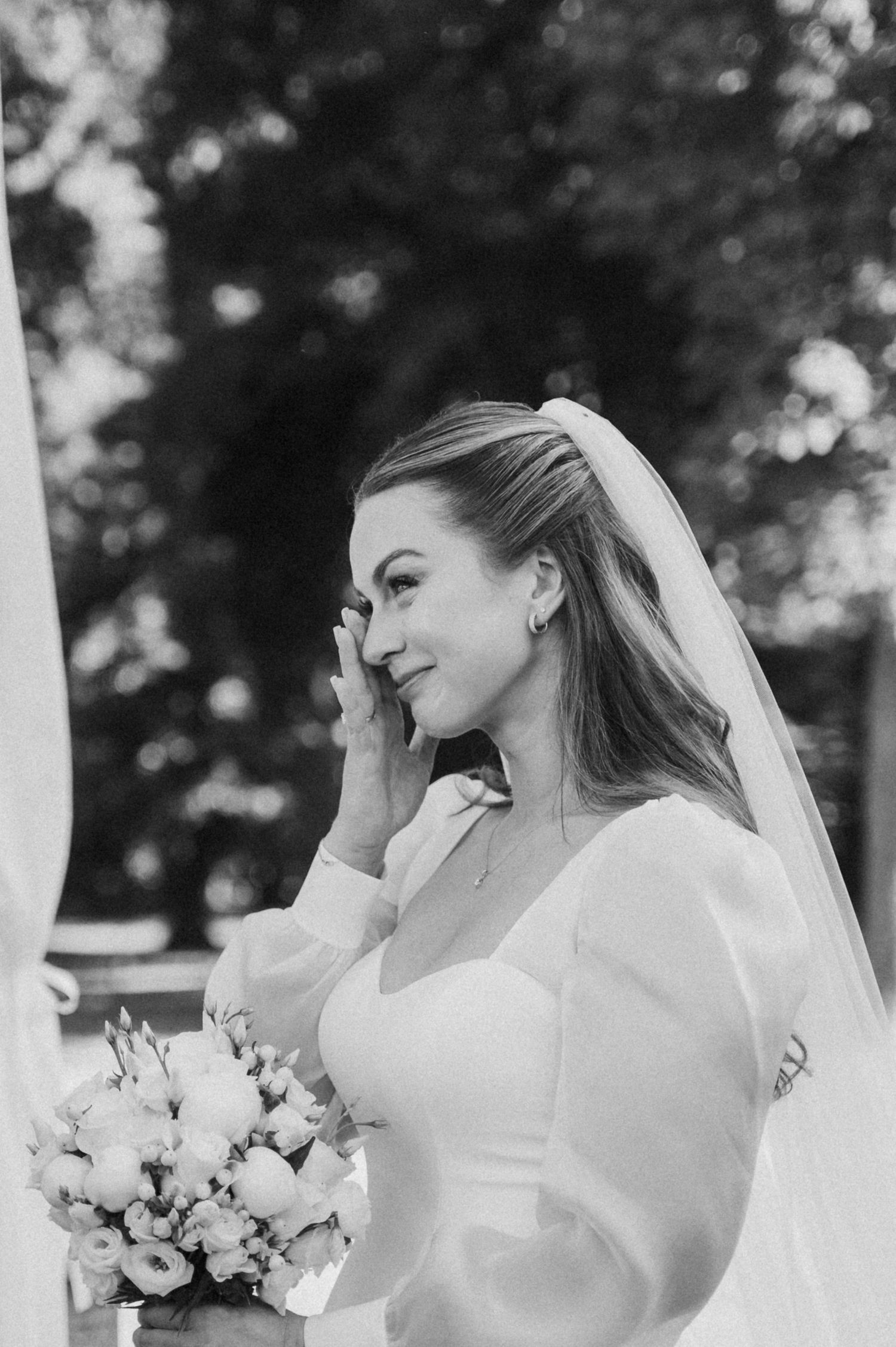 Black and white portrait of a bride in a classic wedding dress with long sleeves holding a floral bouquet.