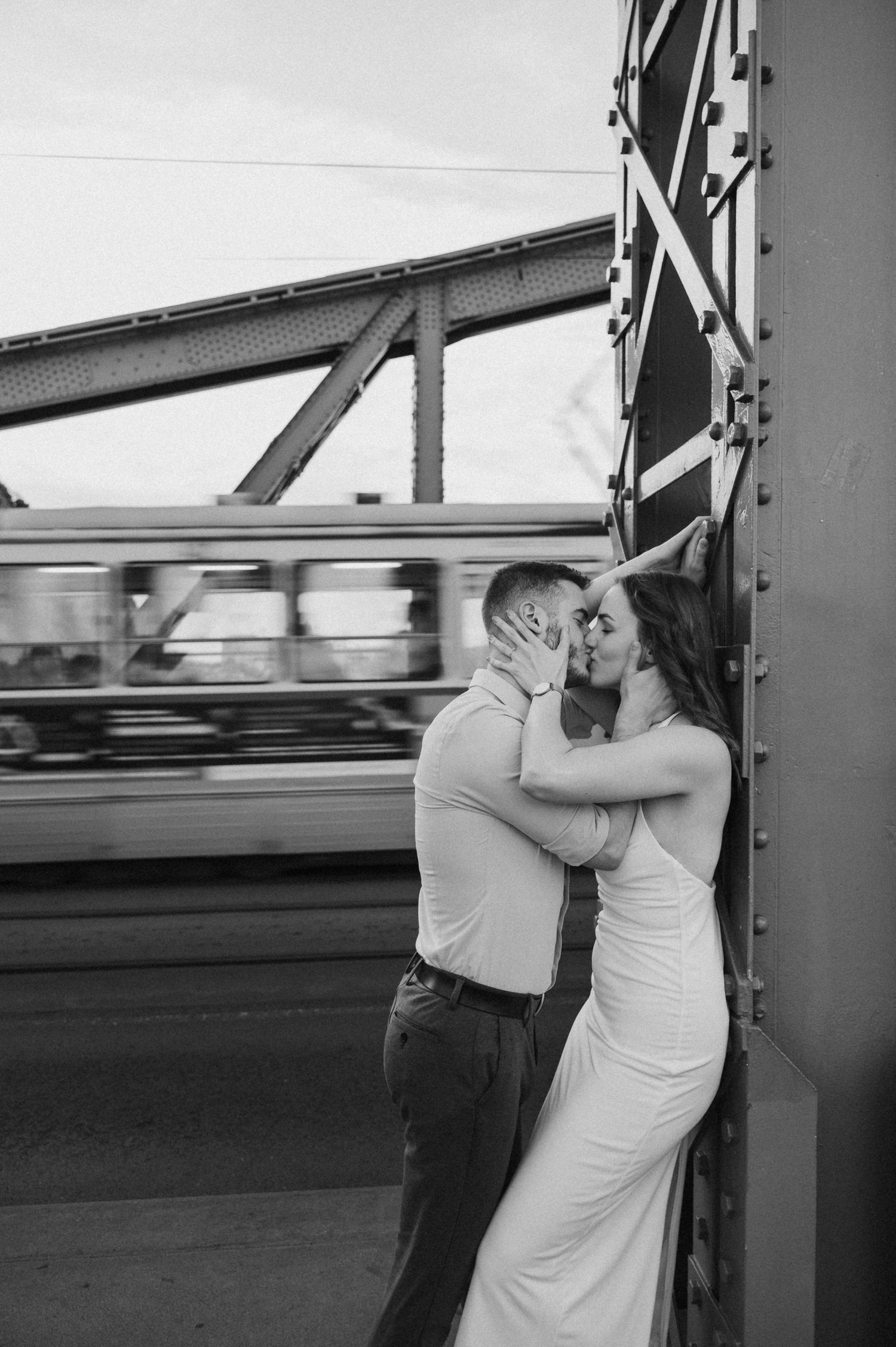 Romantic couple embracing against an industrial backdrop in black and white.
