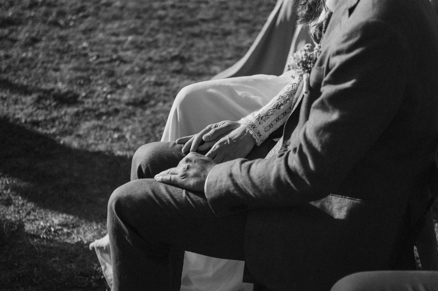 Close-up black and white shot of formal attire and clasped hands during an outdoor event.