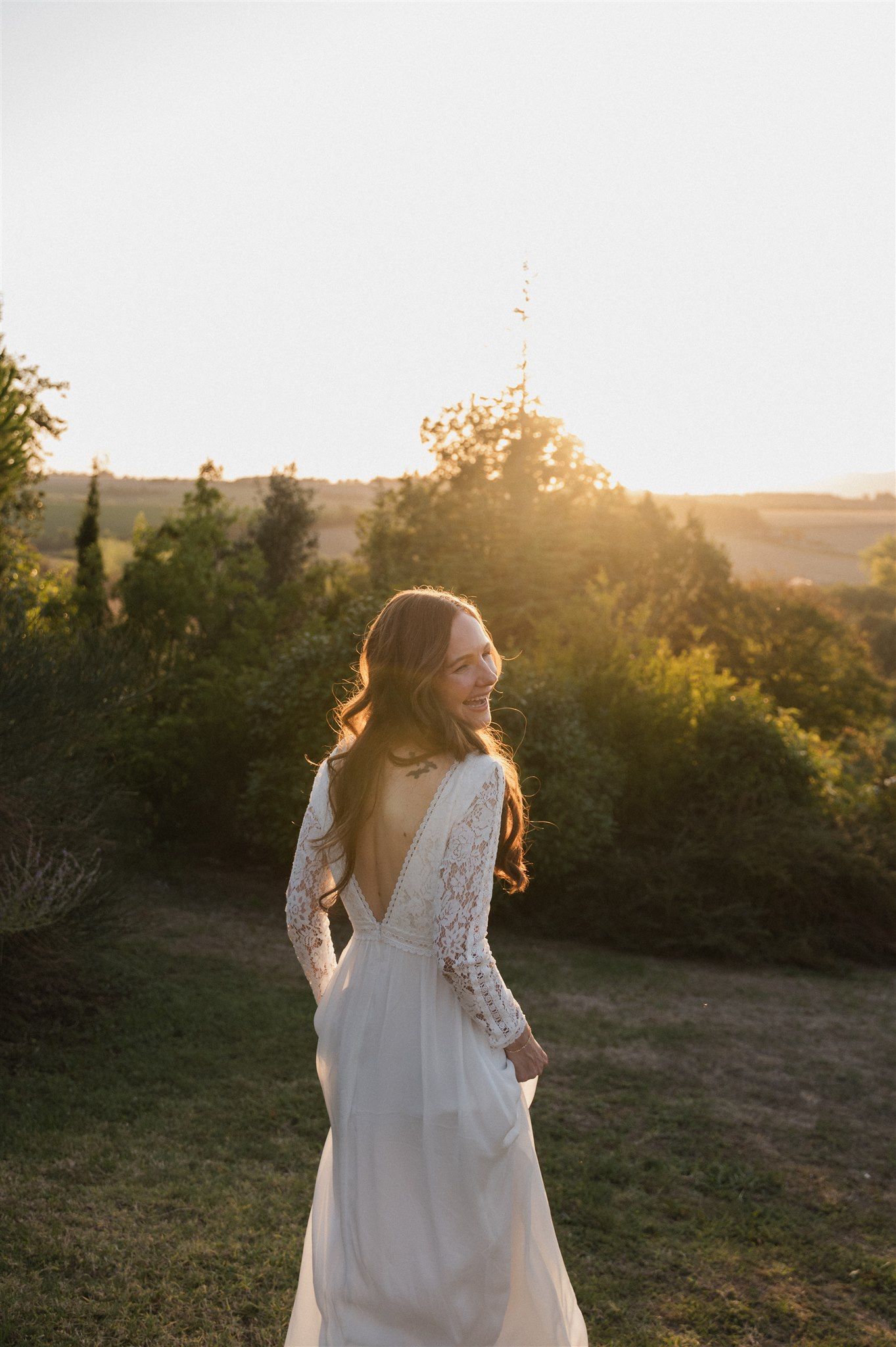 A bride in a lace wedding dress poses in a garden during golden hour sunset.