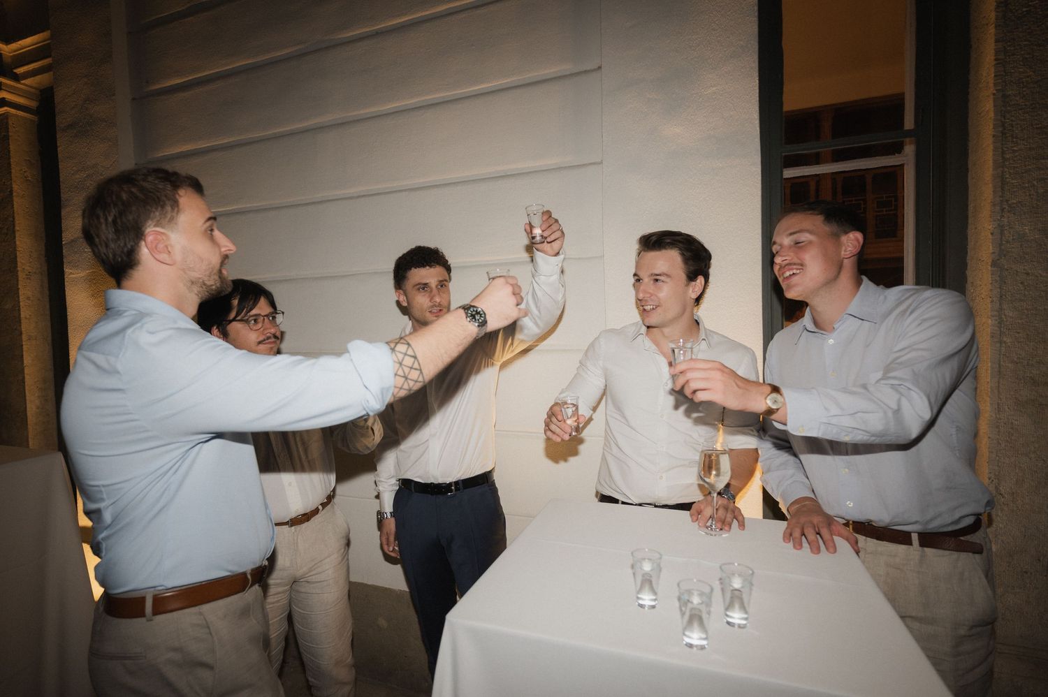 Group of men in dress shirts toasting with champagne glasses at a formal event or wedding reception.