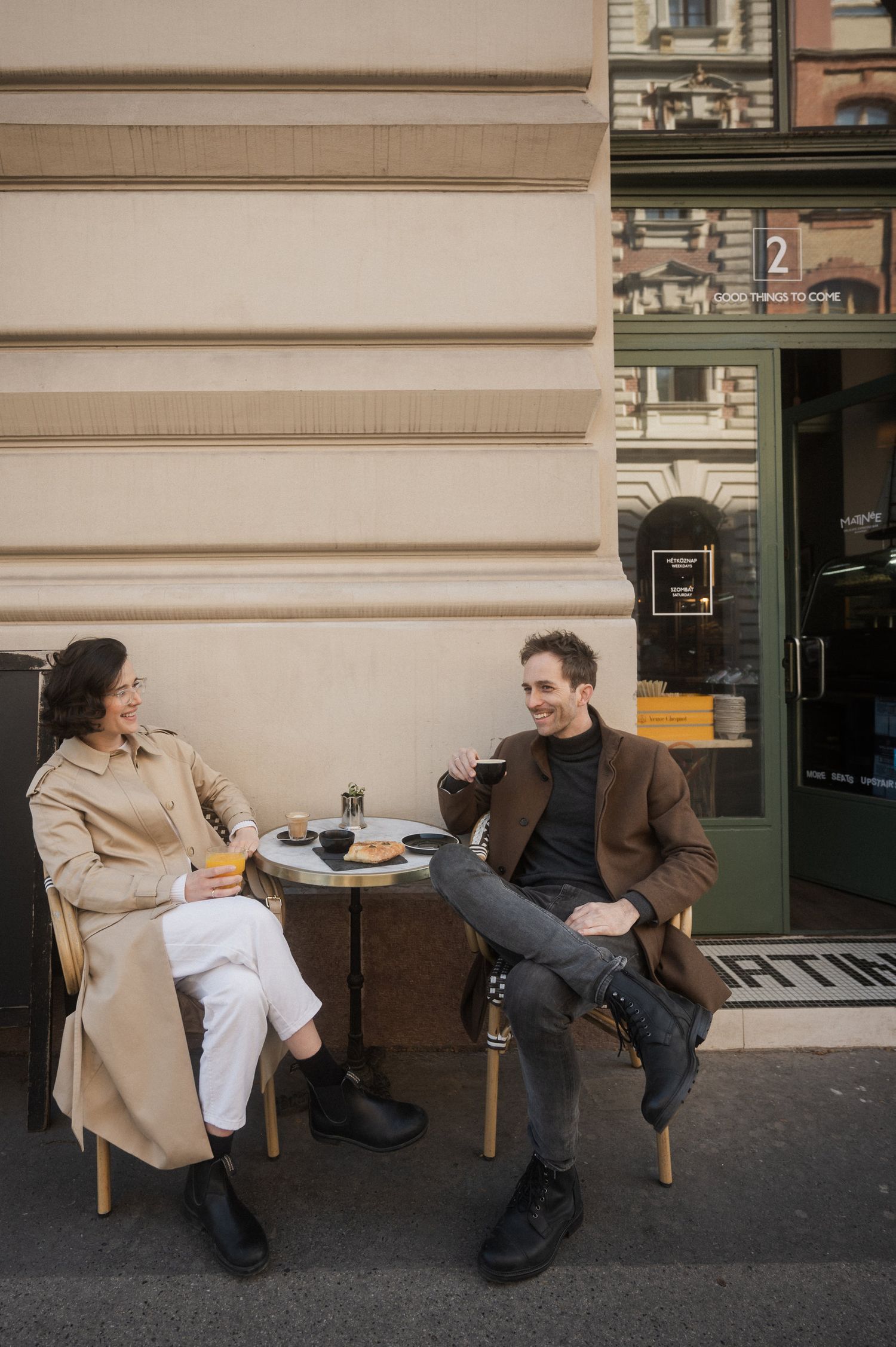 Two people engage in a playful dance sequence on the sidewalk outside a city building.