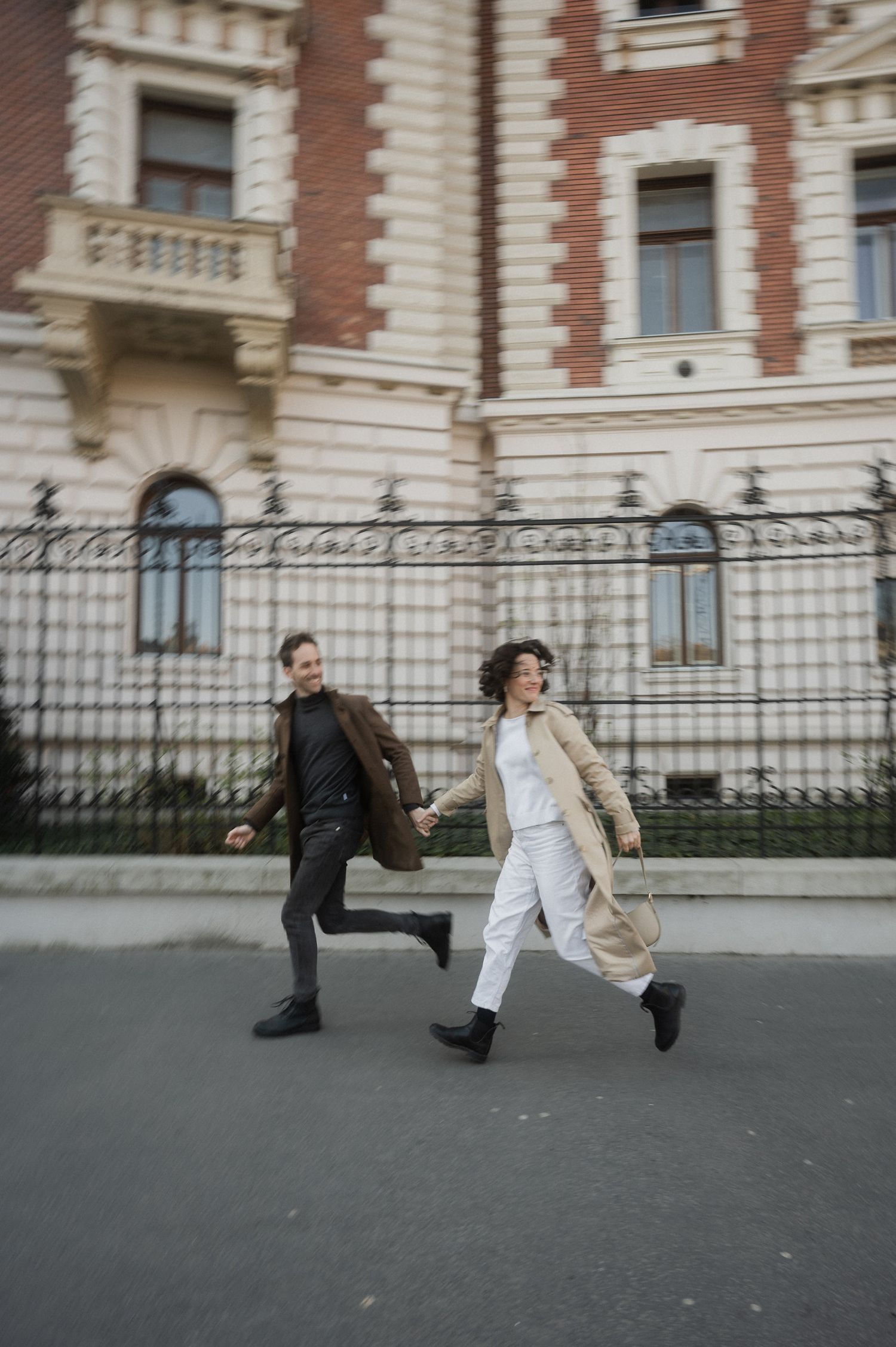 Two people in motion performing a synchronized dance move on a sidewalk outside a brick building.