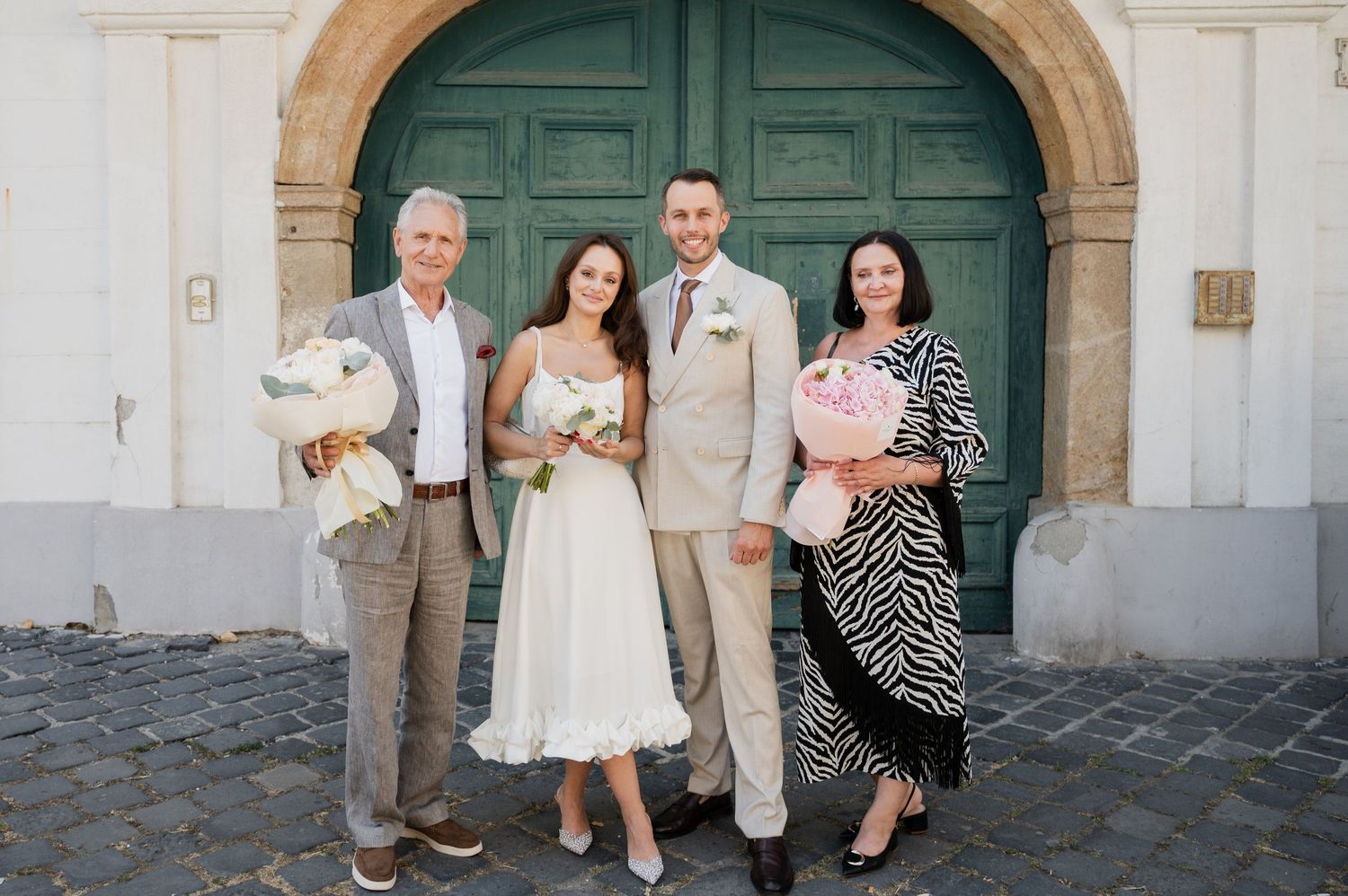 Wedding party poses in front of a large green door and stone archway.