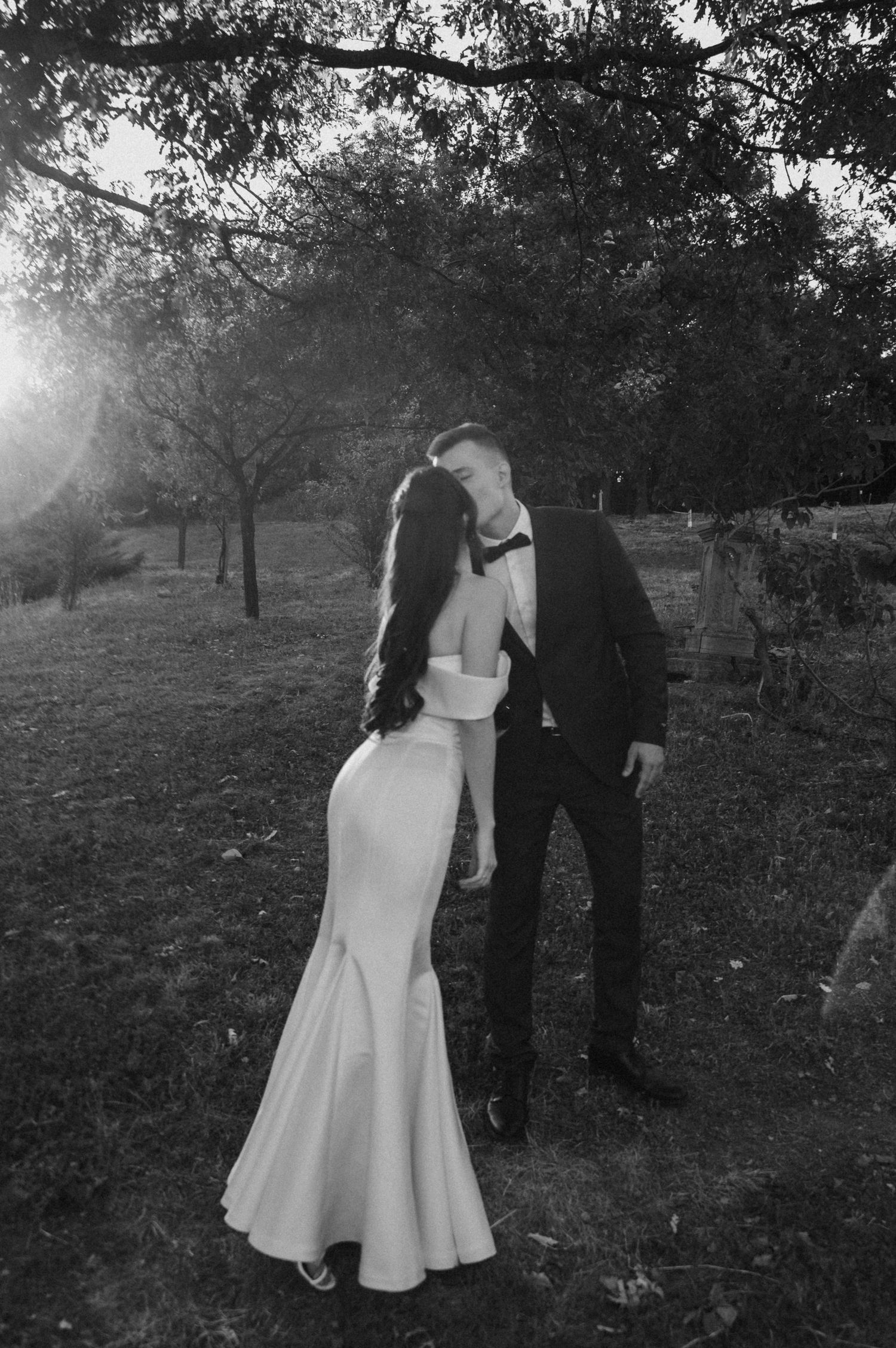 Intimate black and white portrait of newlyweds sharing a moment under trees at dusk.