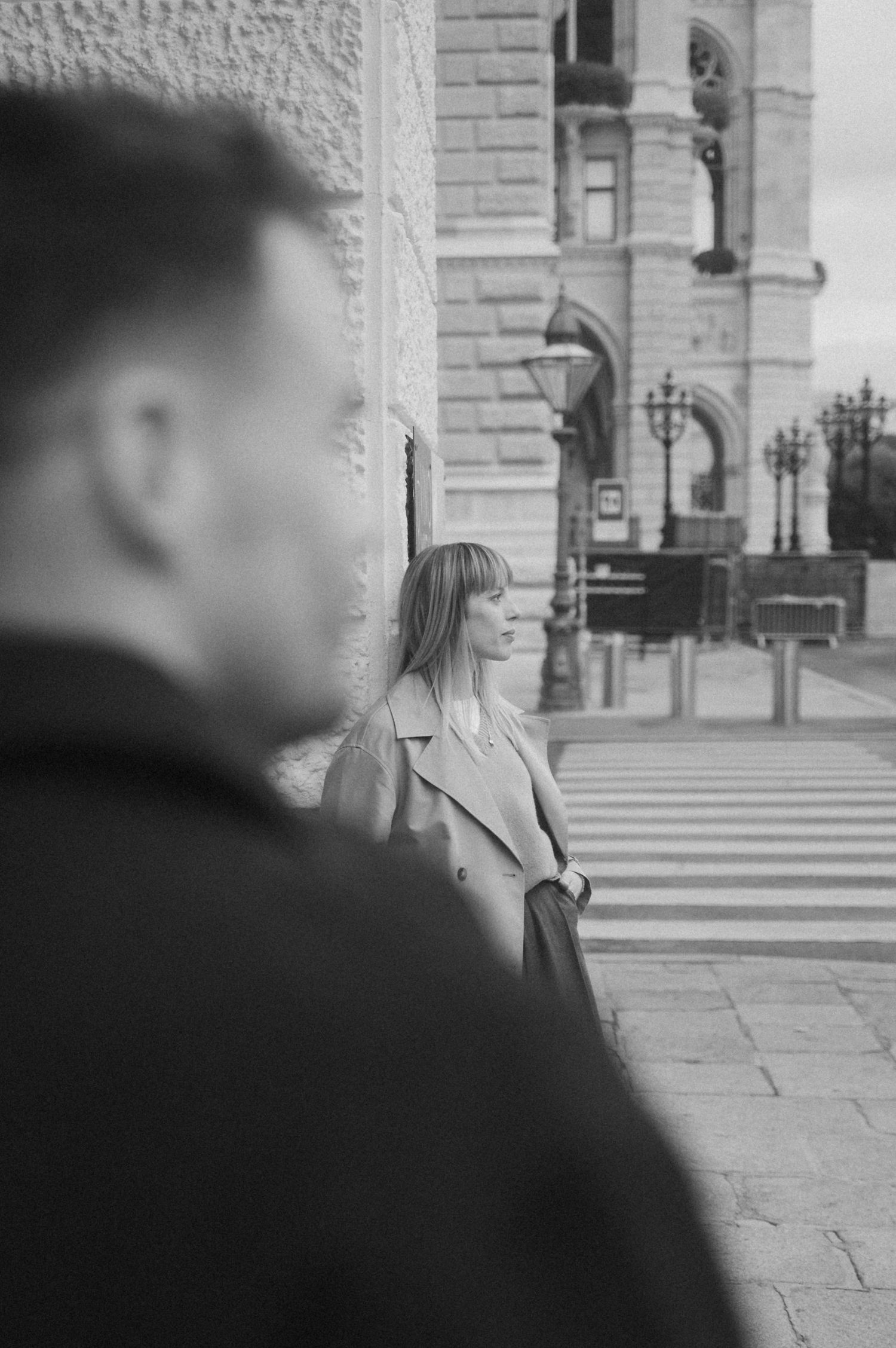 A black and white street scene shows a person in silhouette walking past a stone building exterior.