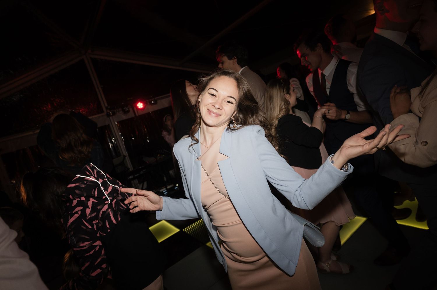 Young woman in a light blue blazer dancing joyfully on the dance floor at a lively wedding reception.