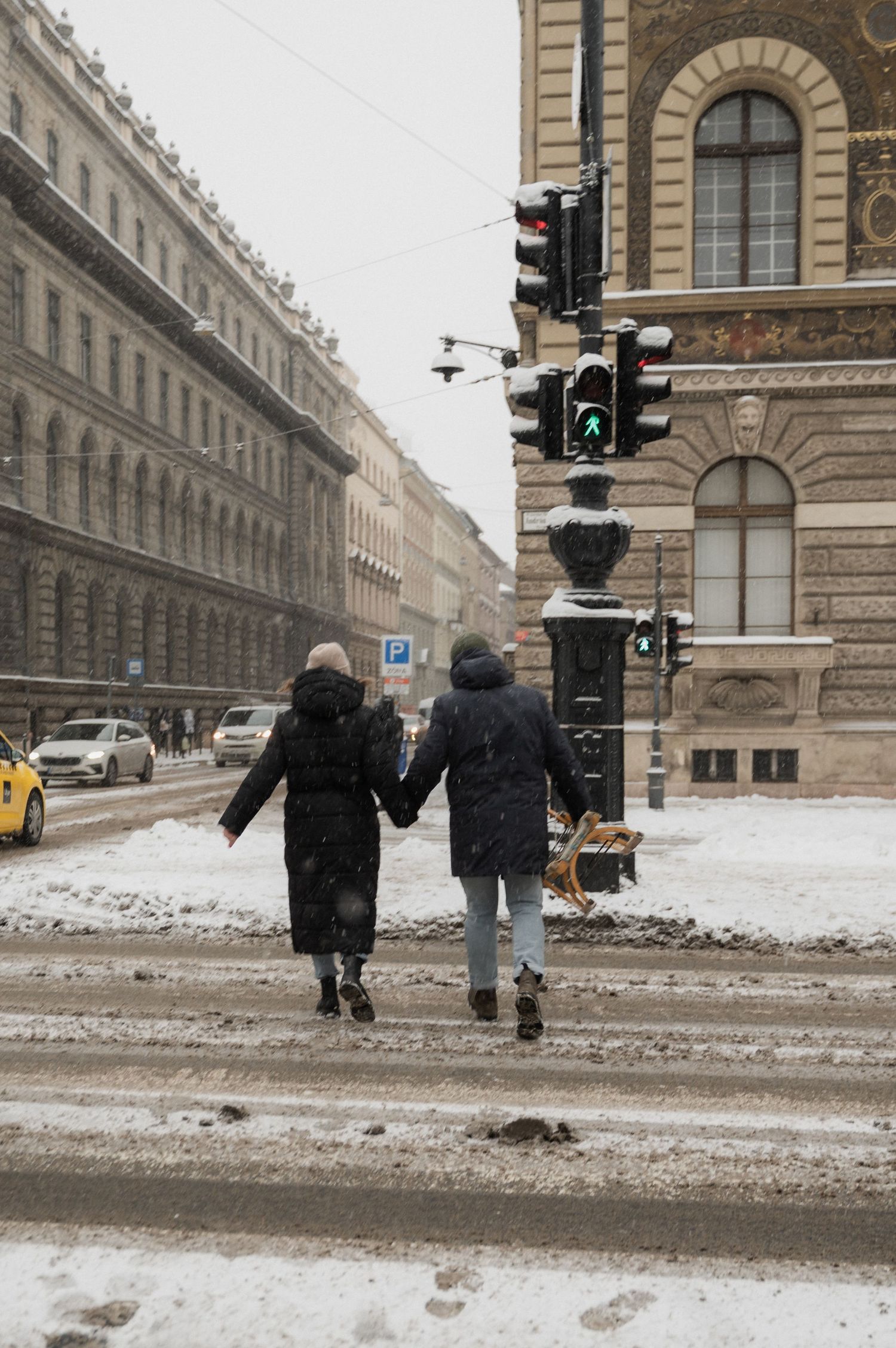 People walking on a snowy street in front of ornate historic architecture.