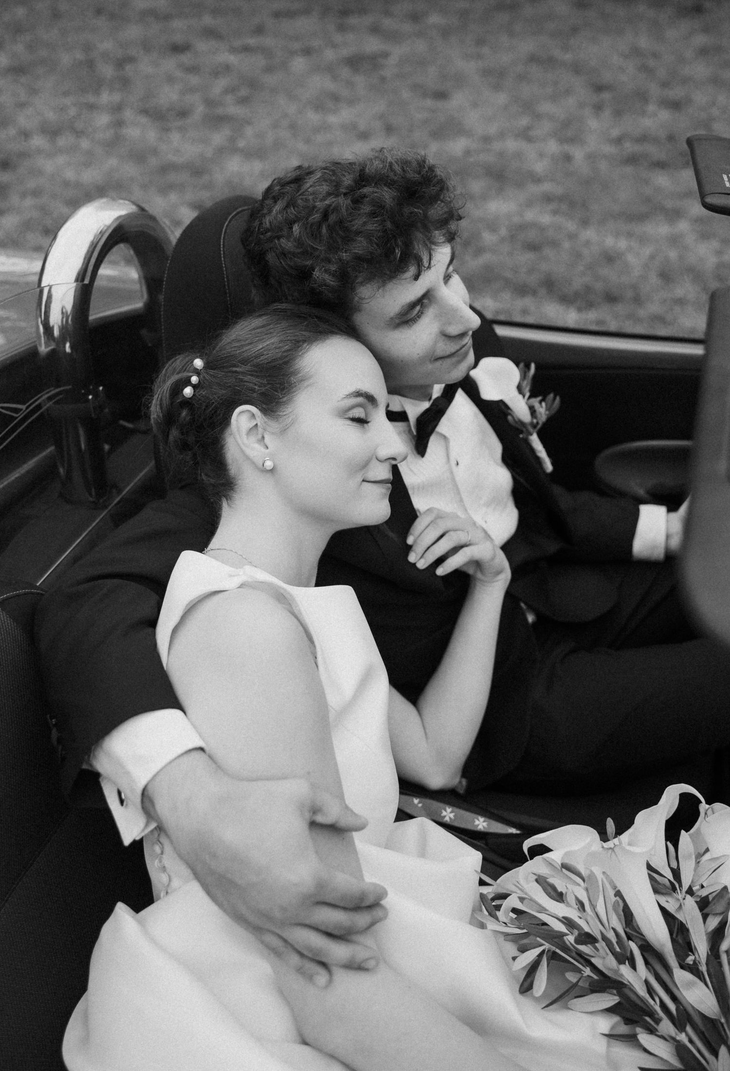 Wedding couple shares intimate moment in classic car during countryside drive.