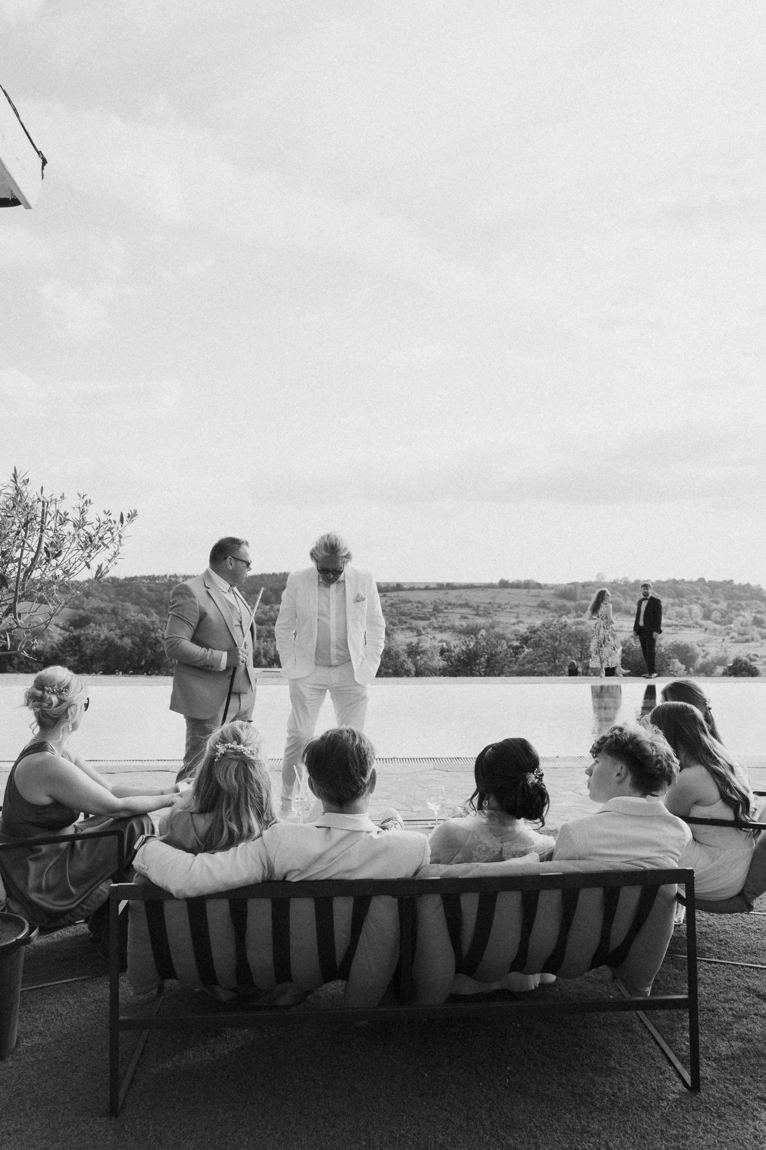 Black and white photo of wedding guests seated watching couple exchange vows outdoors.