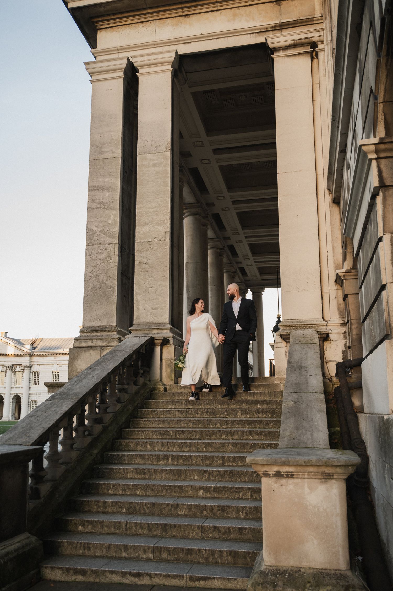 Bride and groom pose on grand stone steps of a historic building.