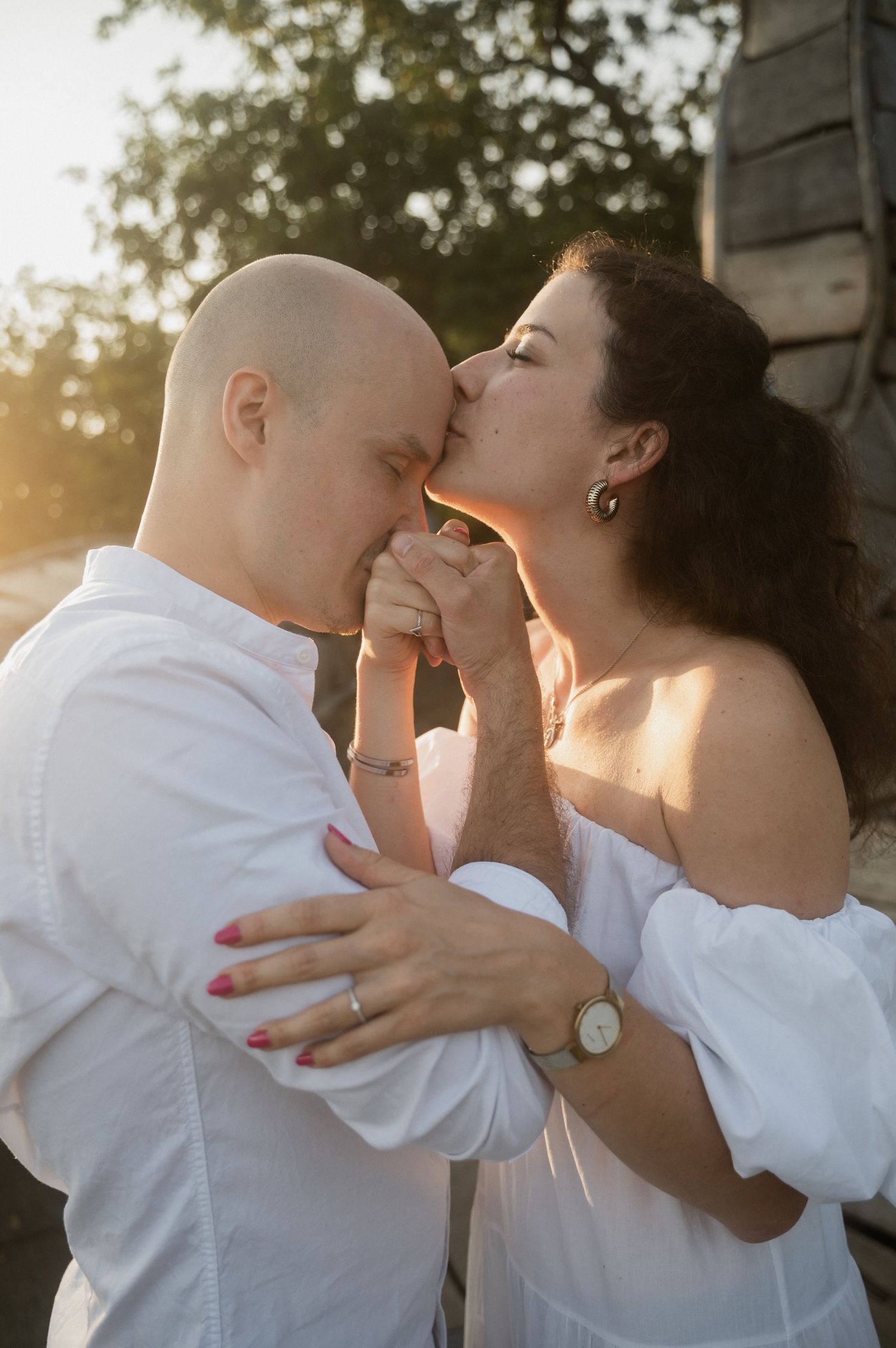 Tender moment between two people in white clothing embracing at sunset in a natural outdoor setting.