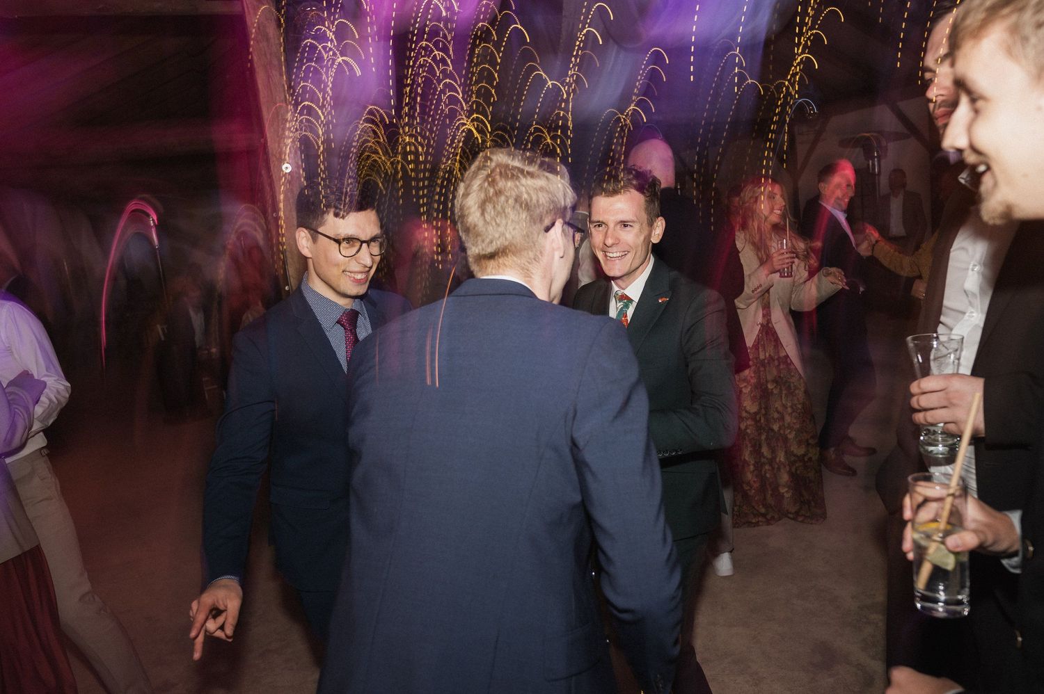 People mingling and socializing at an evening event with purple mood lighting in an indoor venue.
