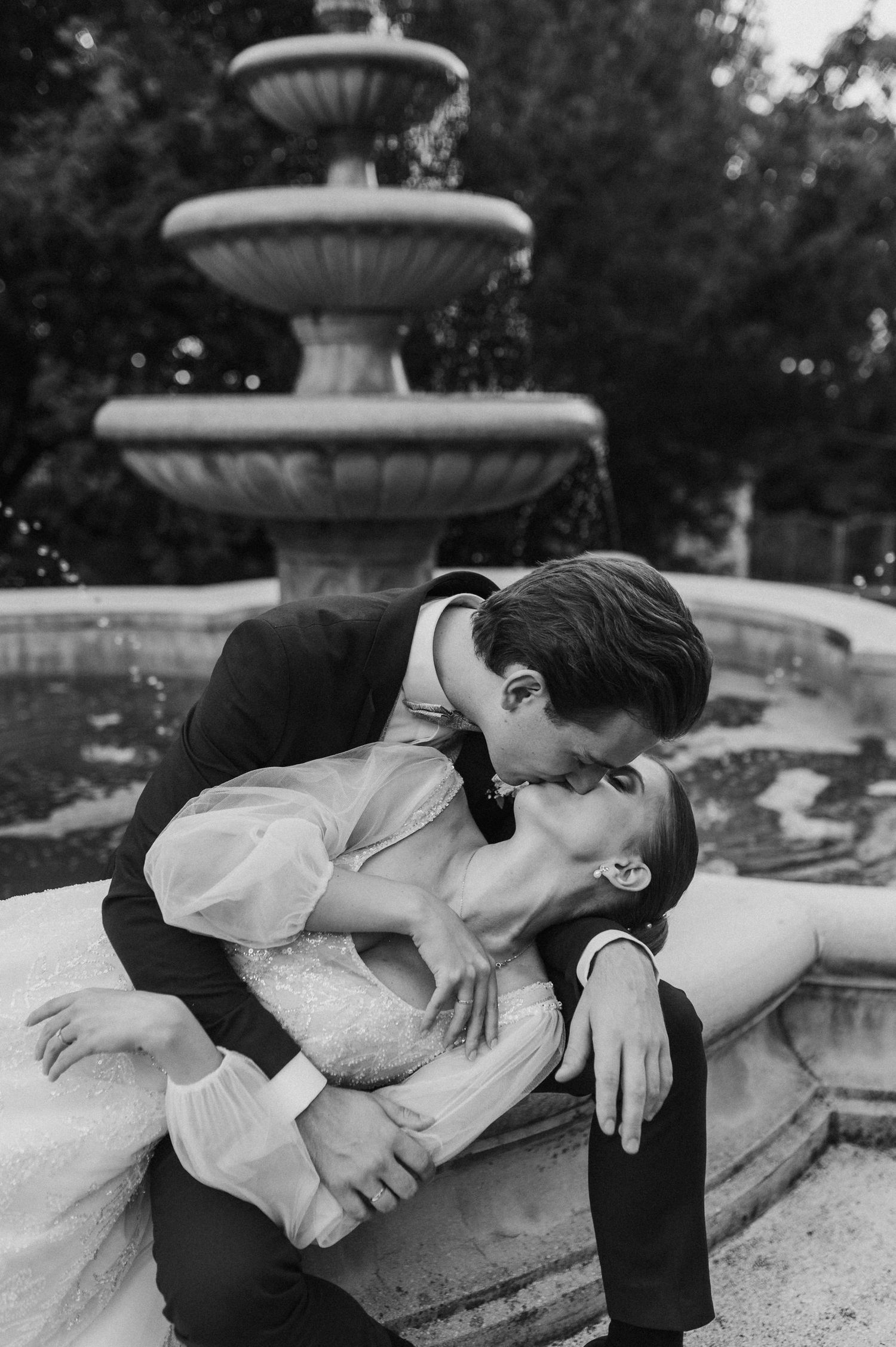 Romantic couple sharing an intimate moment by an ornate stone fountain.