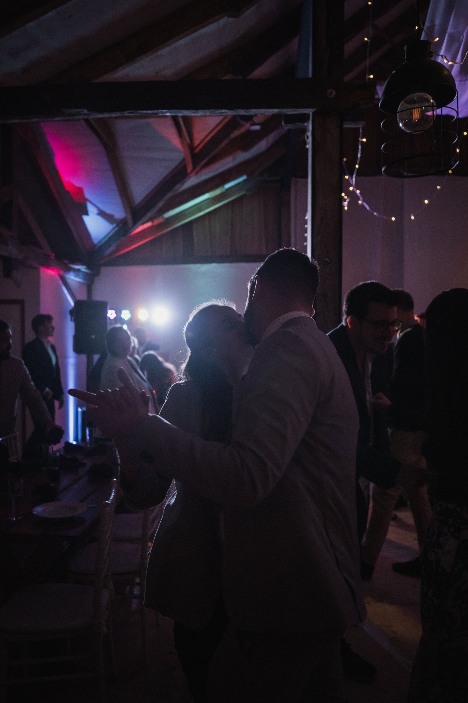 Dark silhouettes of guests moving on a dance floor illuminated by purple and blue stage lighting.