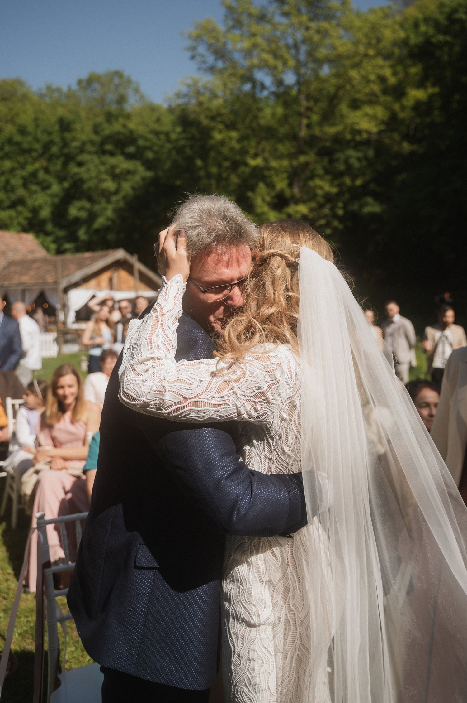 An emotional moment between a bride in a lace dress and groom in a navy suit during an outdoor wedding ceremony.