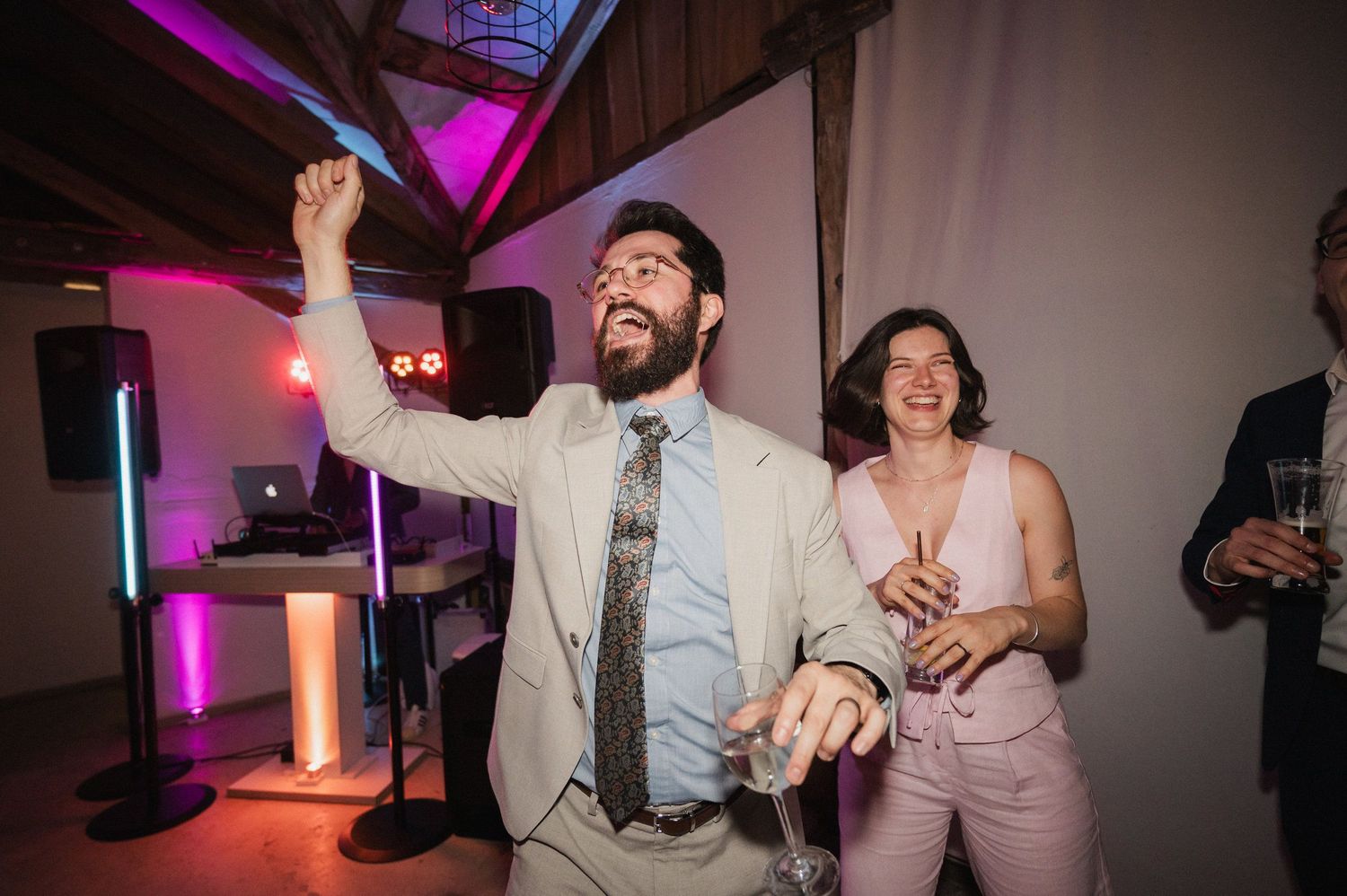 People dancing and celebrating on a dance floor at a wedding reception with purple lighting and festive atmosphere.