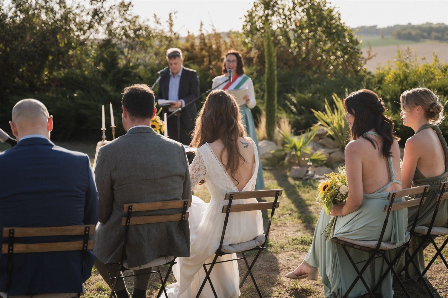 Wedding guests seated at outdoor ceremony during golden hour with natural landscape backdrop.