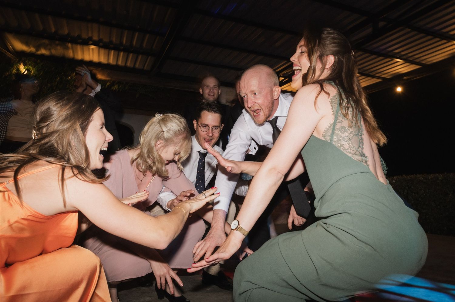 Wedding guests dance together on a dimly lit dance floor during a celebration.