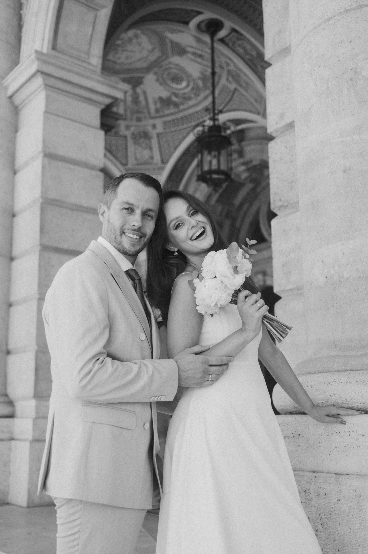Newlyweds share intimate moments against classical architecture backdrop.