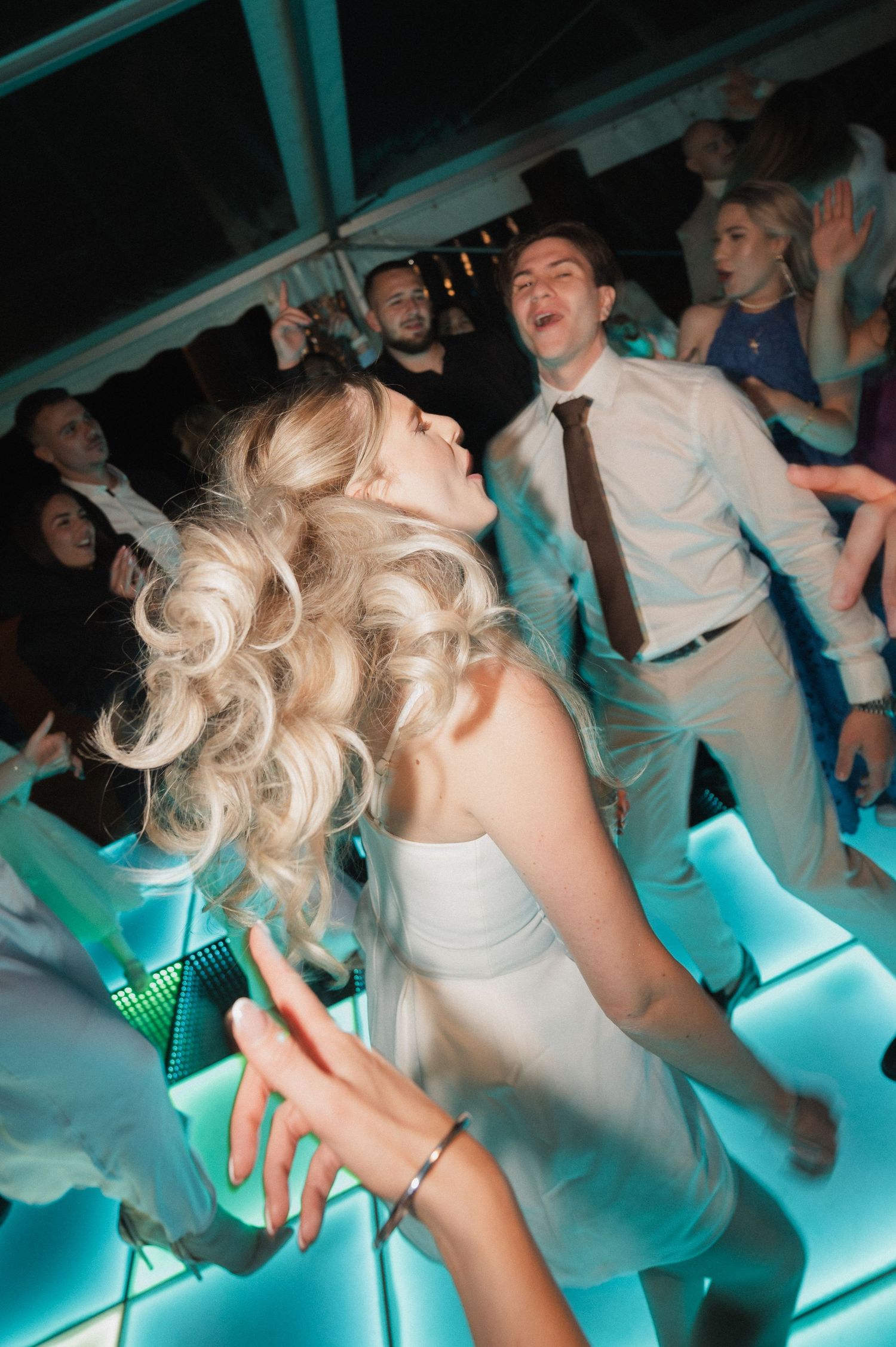 Bride with voluminous blonde curls dancing energetically on a glowing dance floor at her reception.