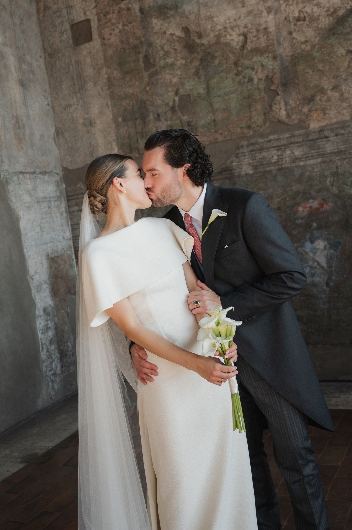 Romantic wedding couple embraces in an atmospheric stone venue.