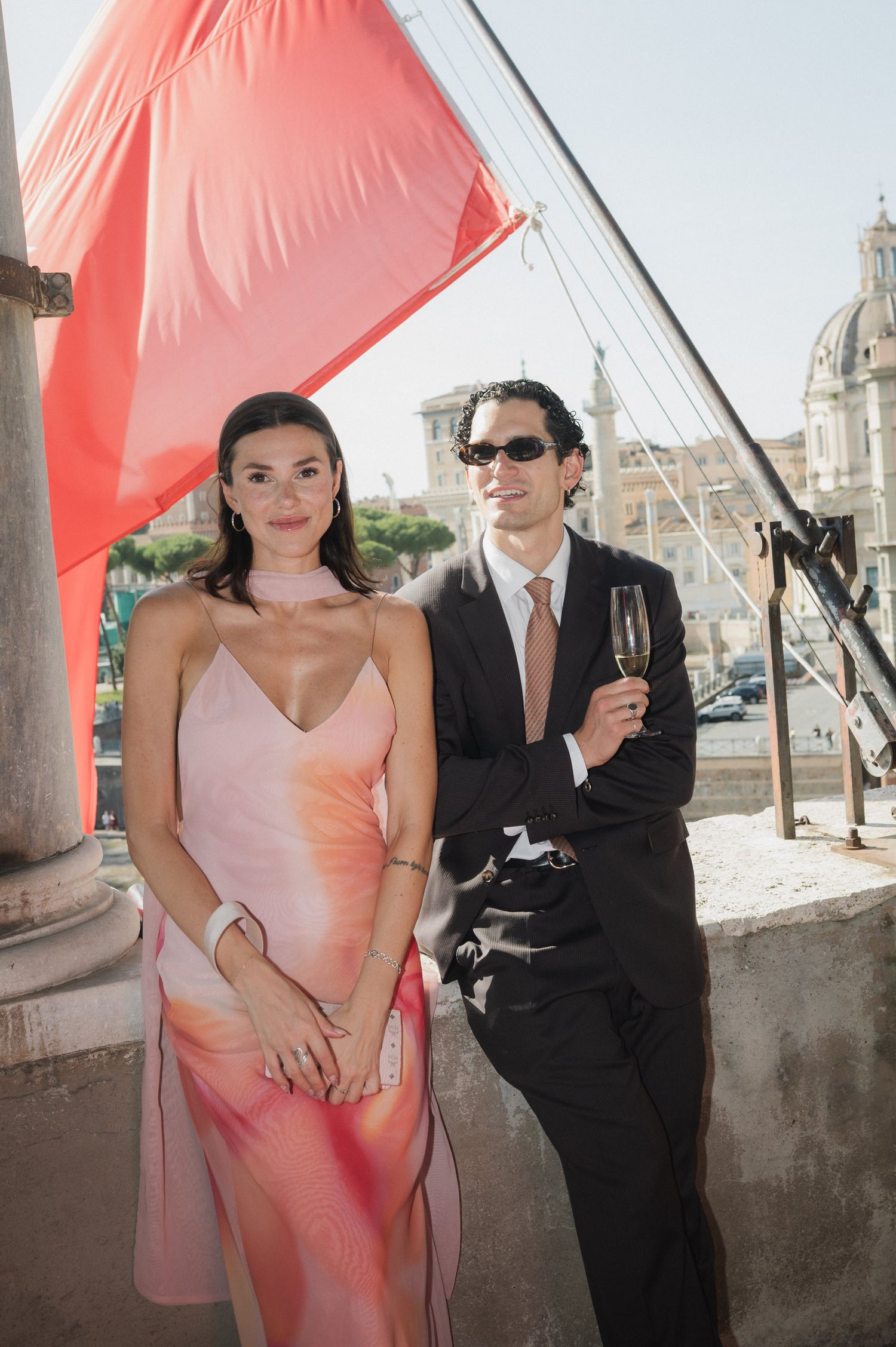 Wedding celebration under stone columns with pink dress and formal attire.