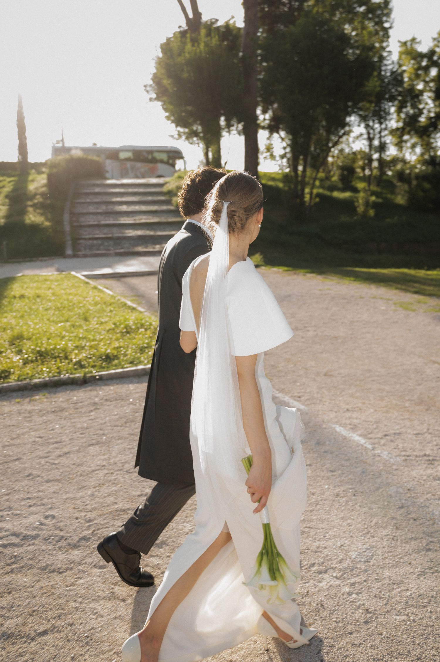 Newlyweds stroll together on a gravel path during golden hour.
